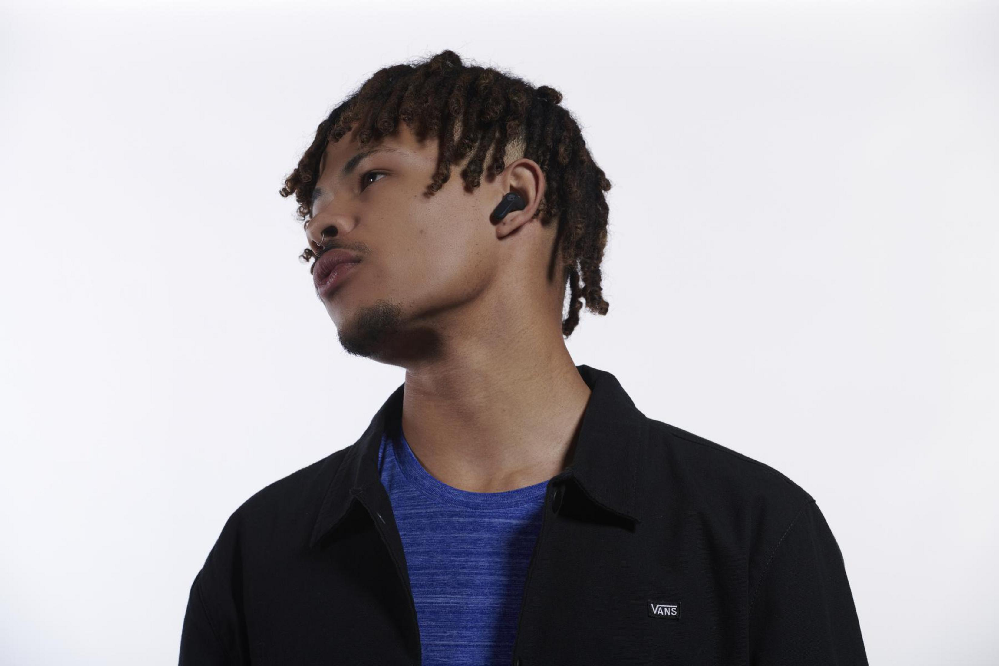 Młody mężczyzna z dredami w słuchawkach, patrzący w lewo. Białe tło.