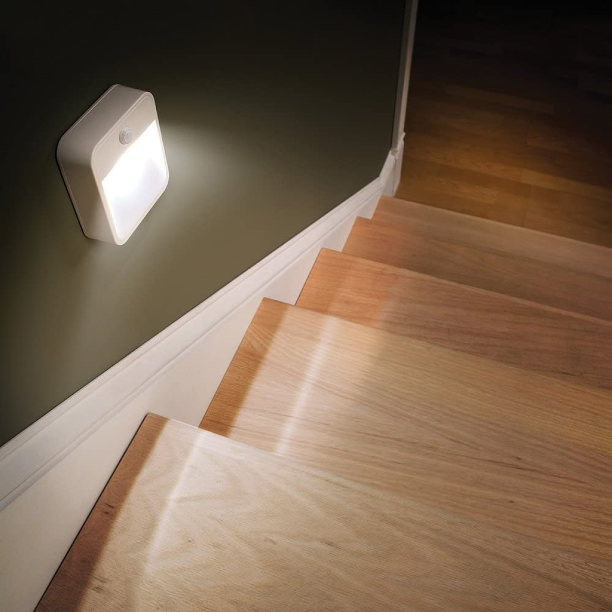 Ein weißes, an der Wand montiertes Nachtlicht an einer Wand neben einer Holztreppe.