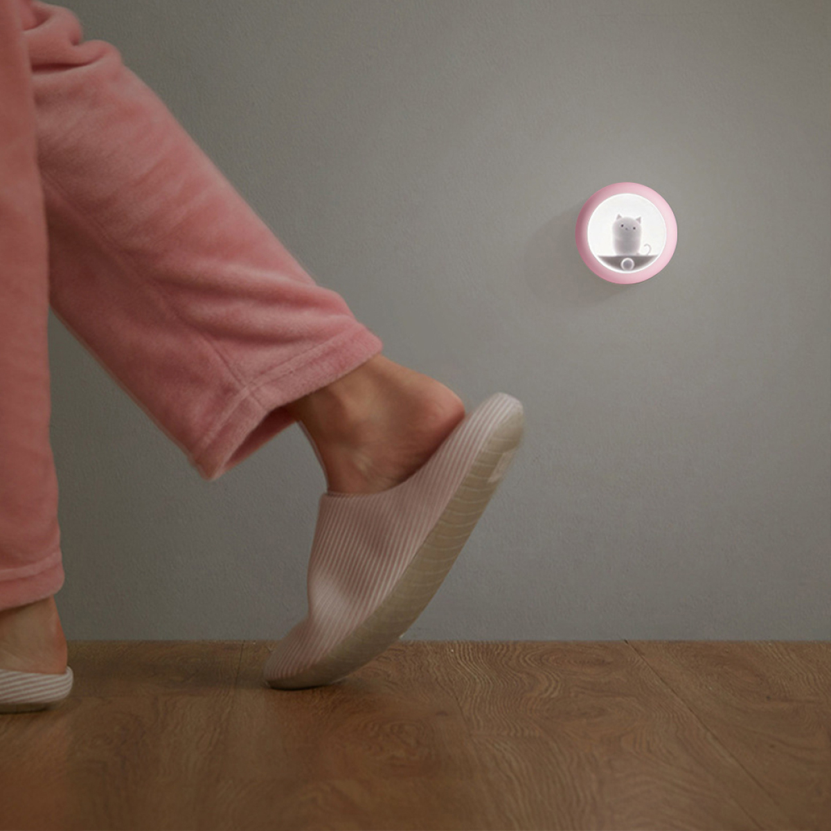 Der Fuß einer Person in einem rosa Pantoffel neben einem Wand-Nachtlicht mit Katzendesign.