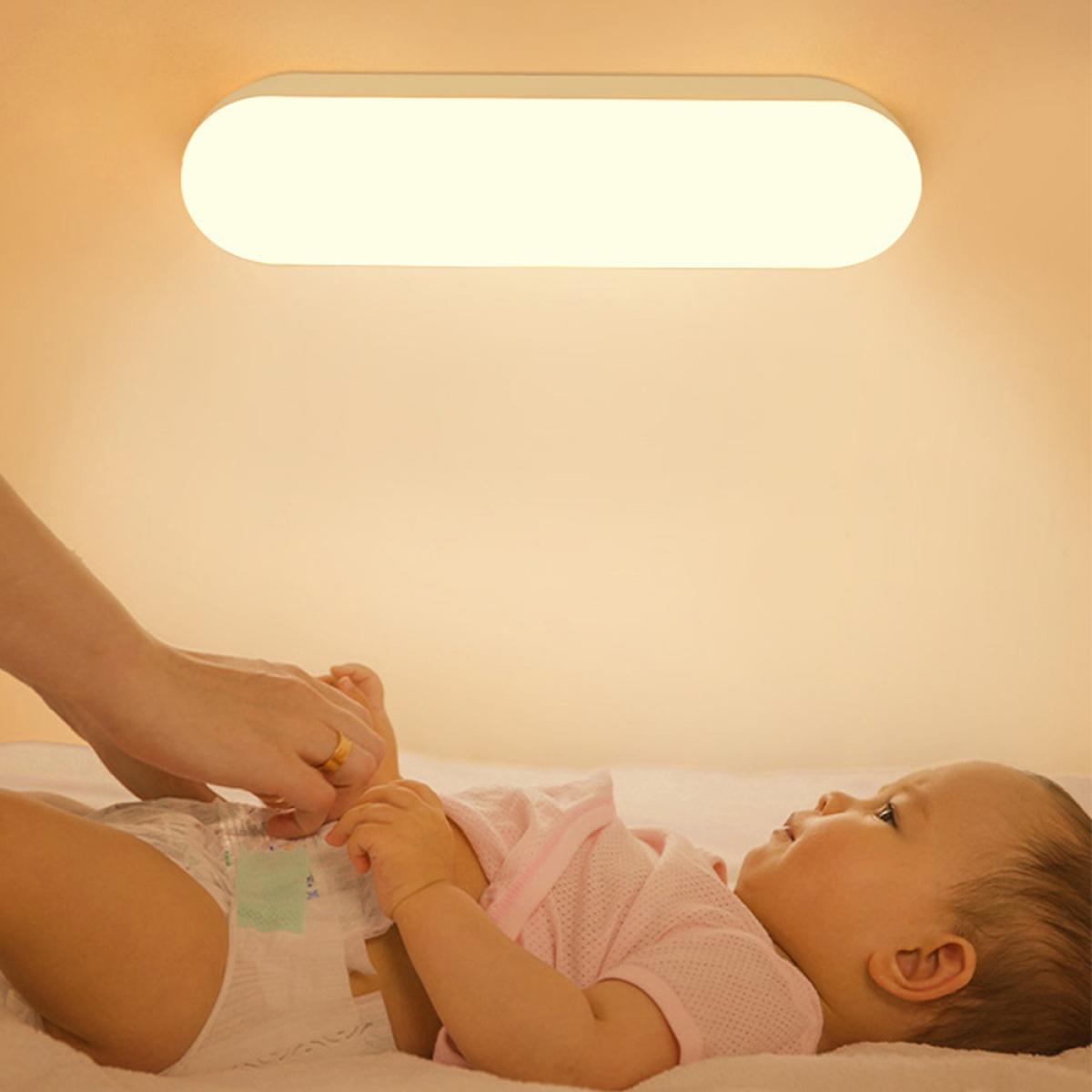 Ein Baby auf einem Bett wird von einem Erwachsenen gewickelt. Eine helle Deckenlampe ist über ihnen.