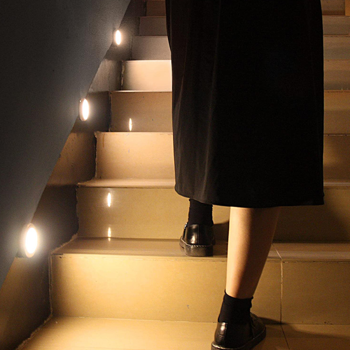 Eine Person, die eine Treppe hinaufgeht, mit Lichtern an der Seite. Die Person trägt ein schwarzes Kleid.