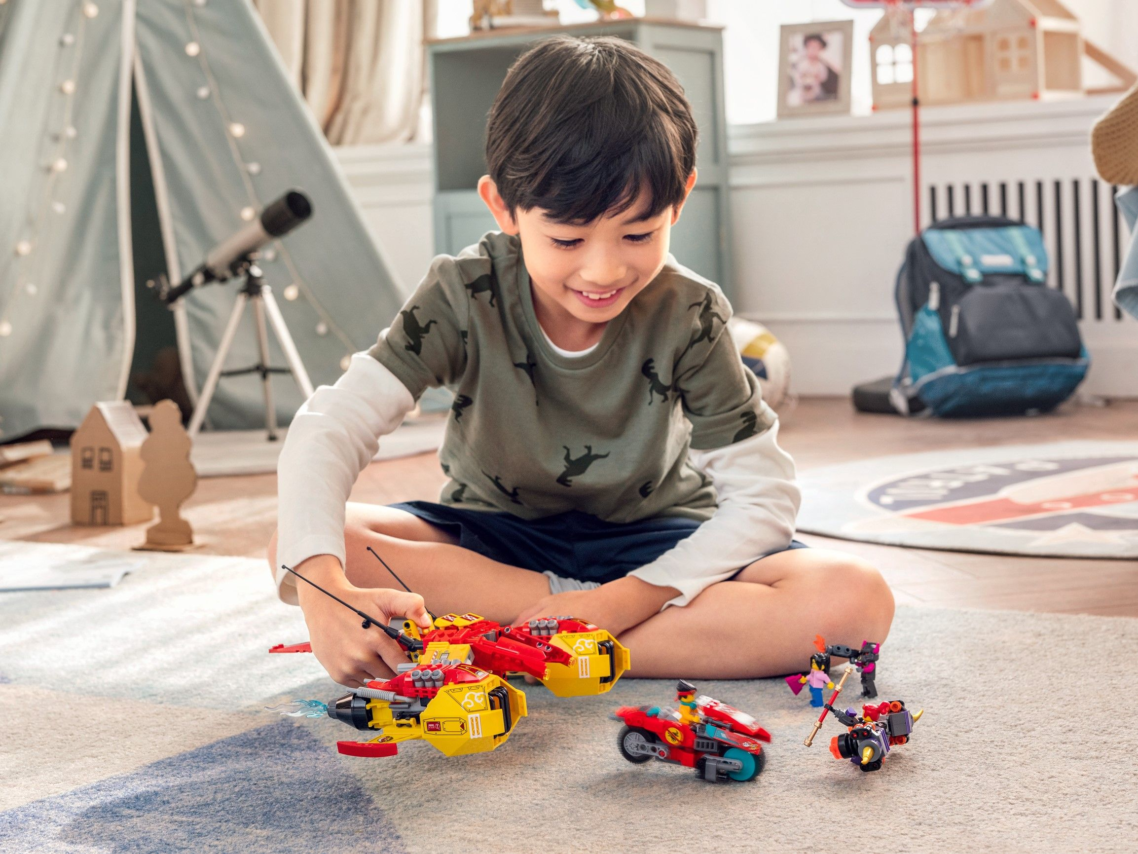 Un bambino gioca con veicoli Lego su un tappeto. Sfondo: tenda e giocattoli.