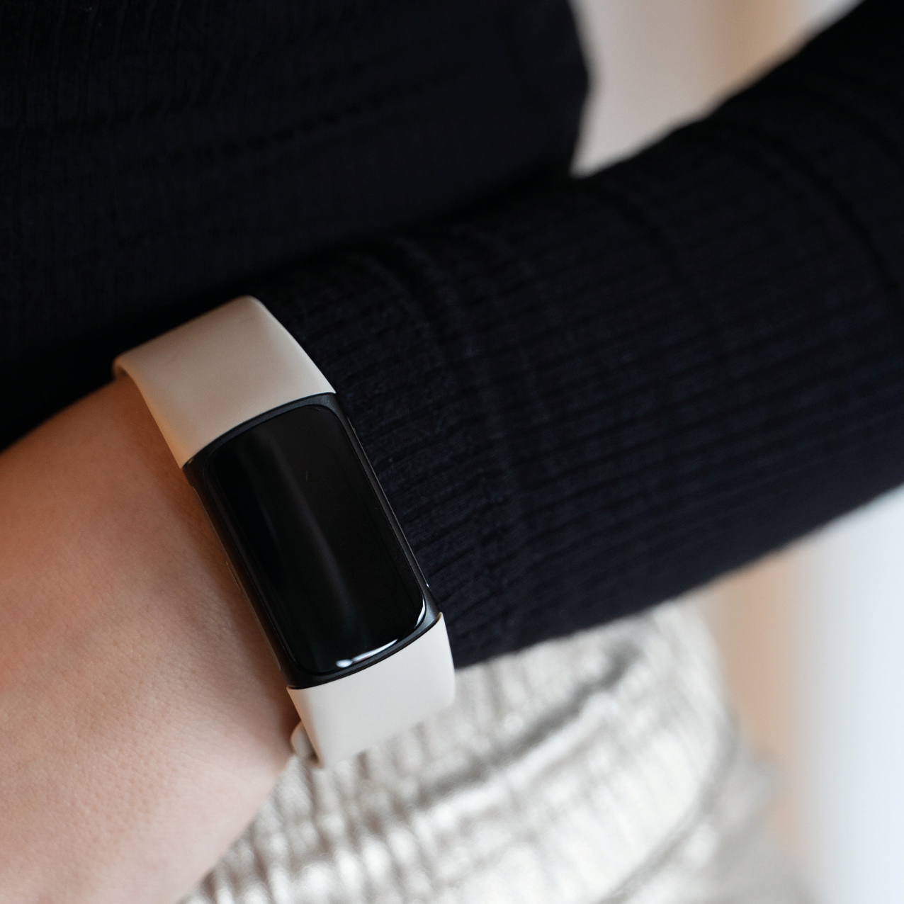 Person trägt einen schwarzen Pullover und einen Fitnesstracker mit schwarzem Bildschirm und weißem Band.