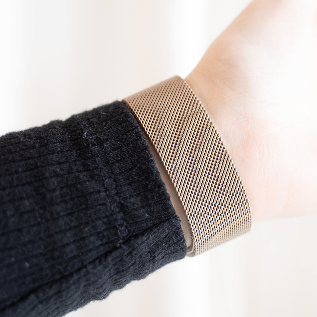 Nahaufnahme eines Handgelenks mit goldenem Mesh-Armband. Schwarzer Ärmel. Weißer Hintergrund. Elegant und stilvoll.