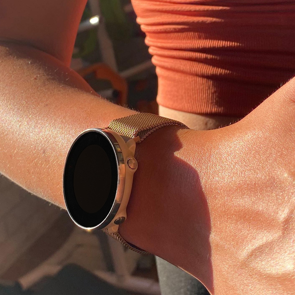 Handgelenk einer Frau mit goldener Uhr mit schwarzem Bildschirm. Die Uhr ist an einem goldenen Mesh-Armband. Der Hintergrund ist hell.