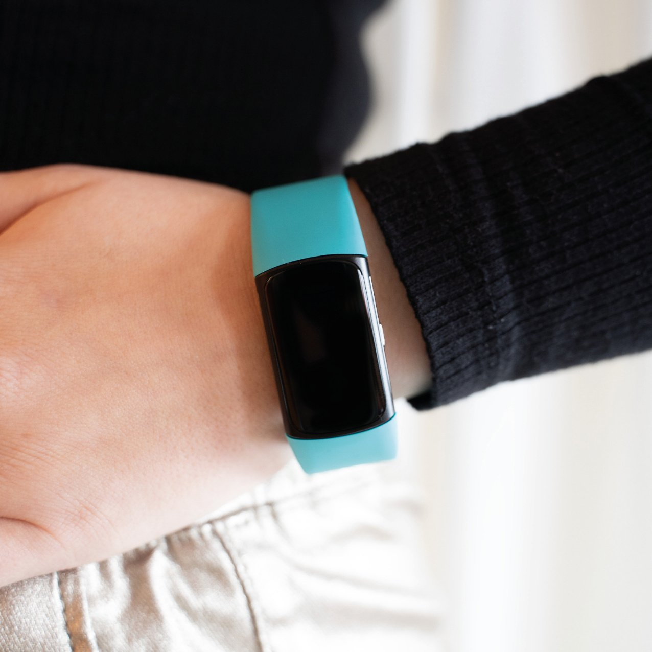 Das Handgelenk einer Person mit einem türkisfarbenen Fitness-Tracker.