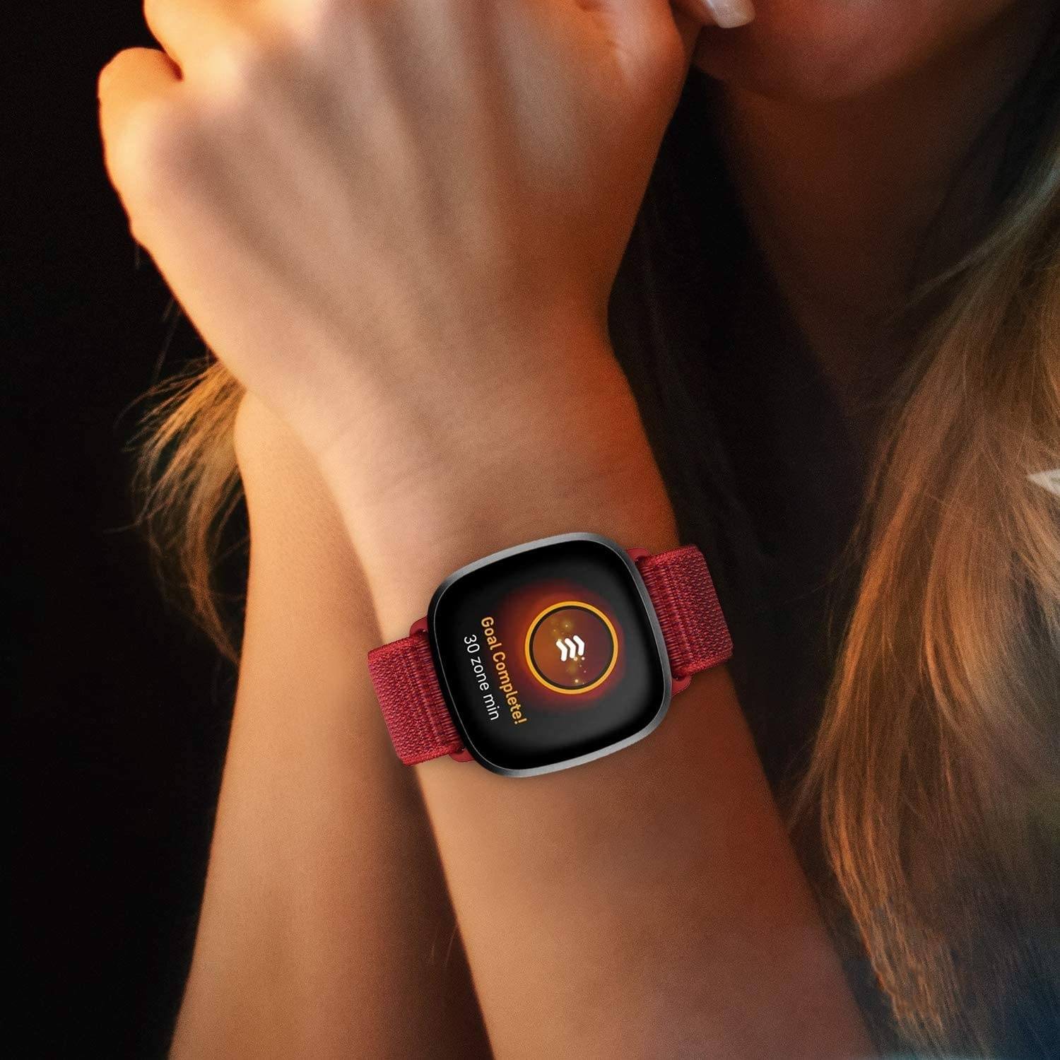 Eine Smartwatch am Handgelenk. Die Uhr zeigt eine Meldung 'Ziel erreicht', mit einem roten gewebten Armband.