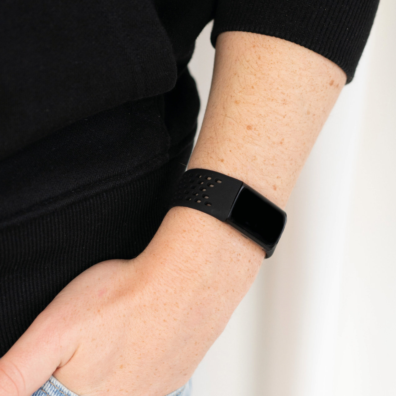 Eine Person, die ein schwarzes Uhrenarmband am Handgelenk trägt. Die Uhr hat einen schwarzen Bildschirm.