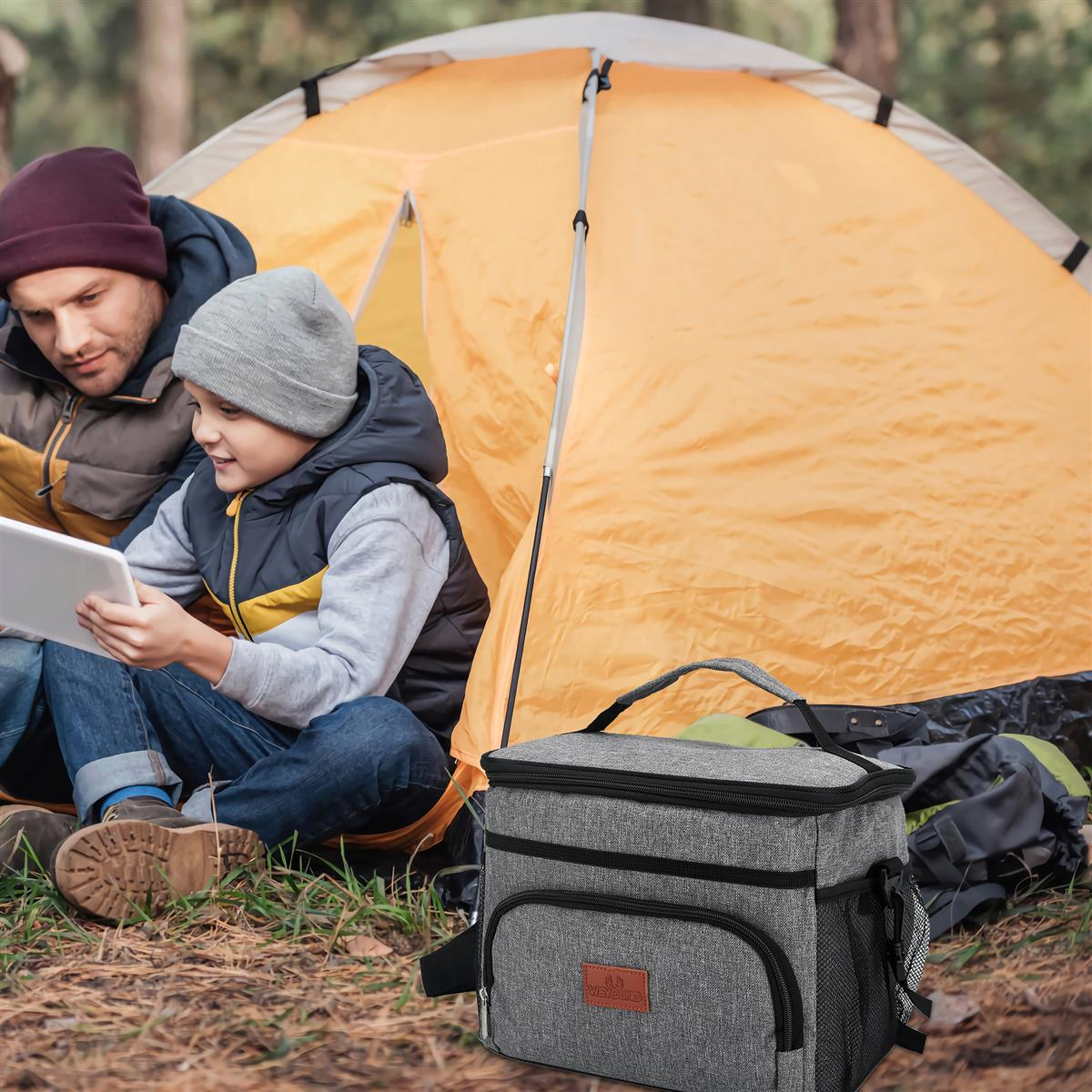 Vater und Sohn schauen vor einem Zelt auf ein Tablet, im Vordergrund eine graue Kühltasche.