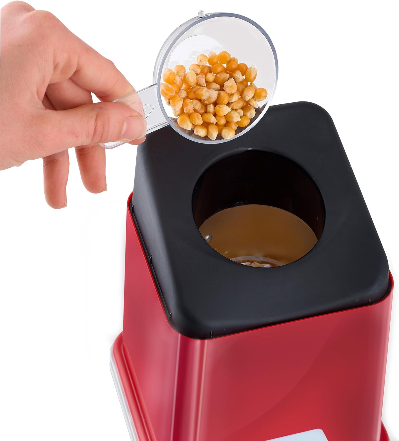 Eine Hand gießt Popcornkörner aus einer Schaufel in einen roten Popcornmacher.
