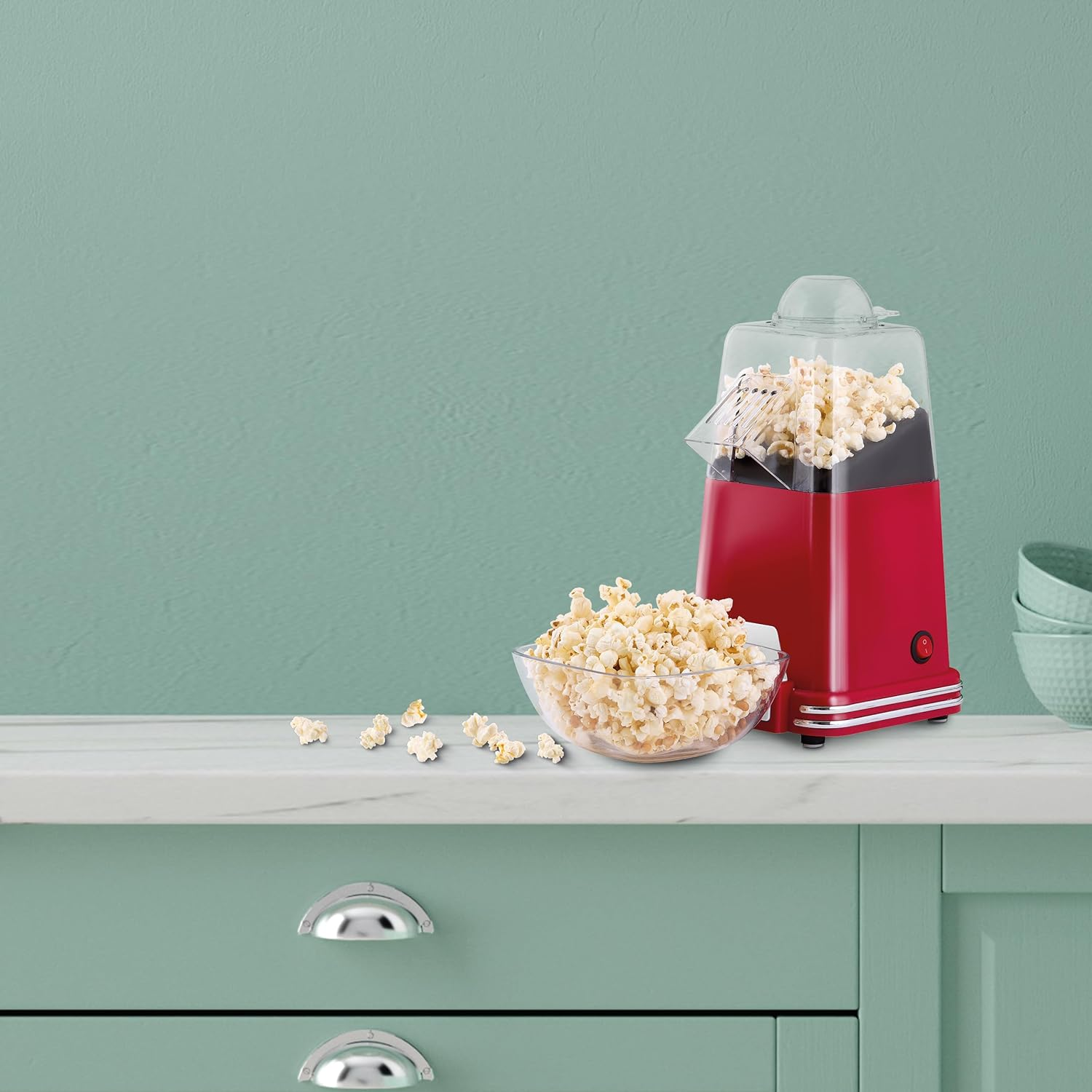 Roter Popcorn-Maker mit Popcorn in einer Glasschüssel. Im Hintergrund eine grüne Theke.