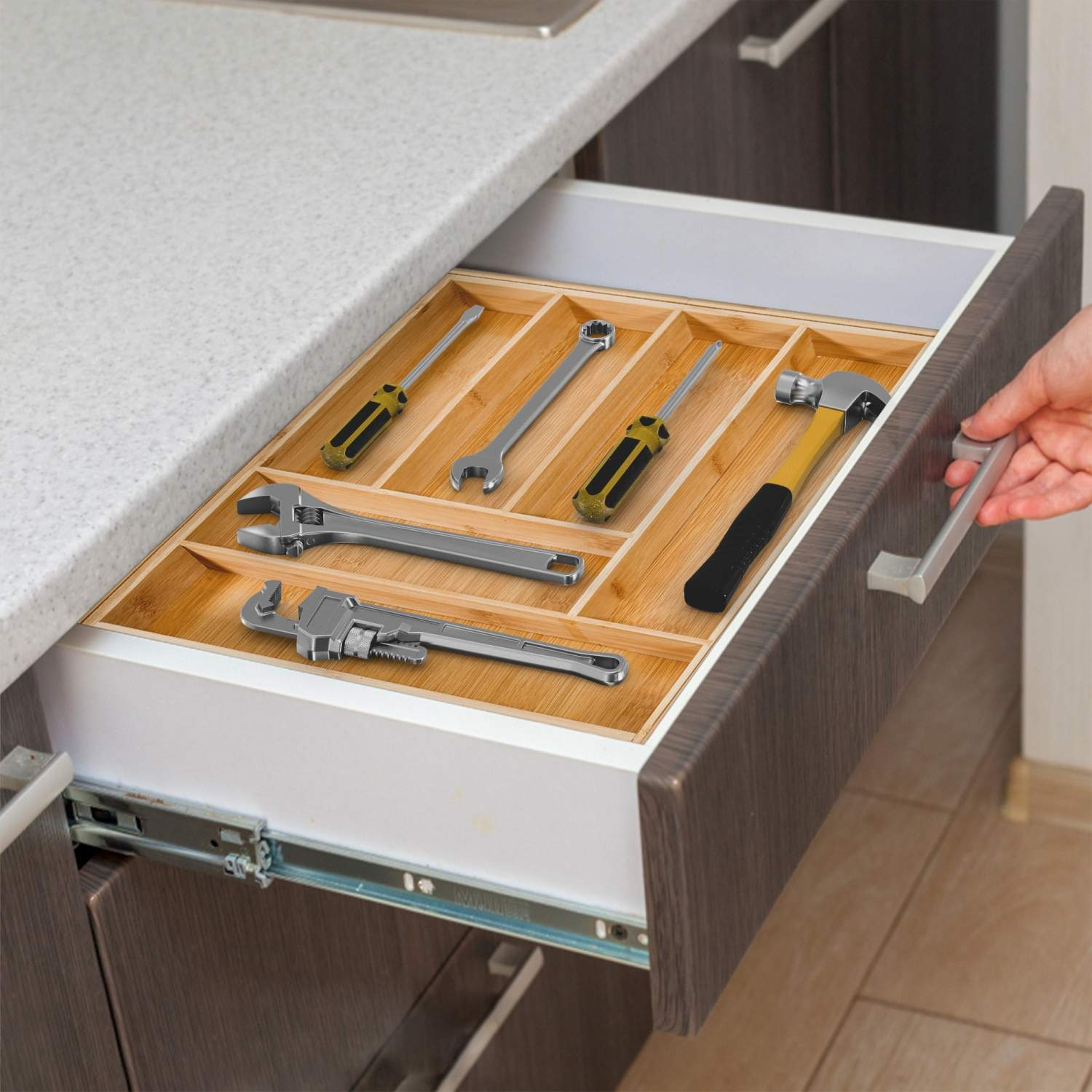Geöffnete Küchenschublade mit Werkzeugen, darunter Schraubendreher, Schraubenschlüssel und ein Hammer. Eine Hand zieht die Schublade.
