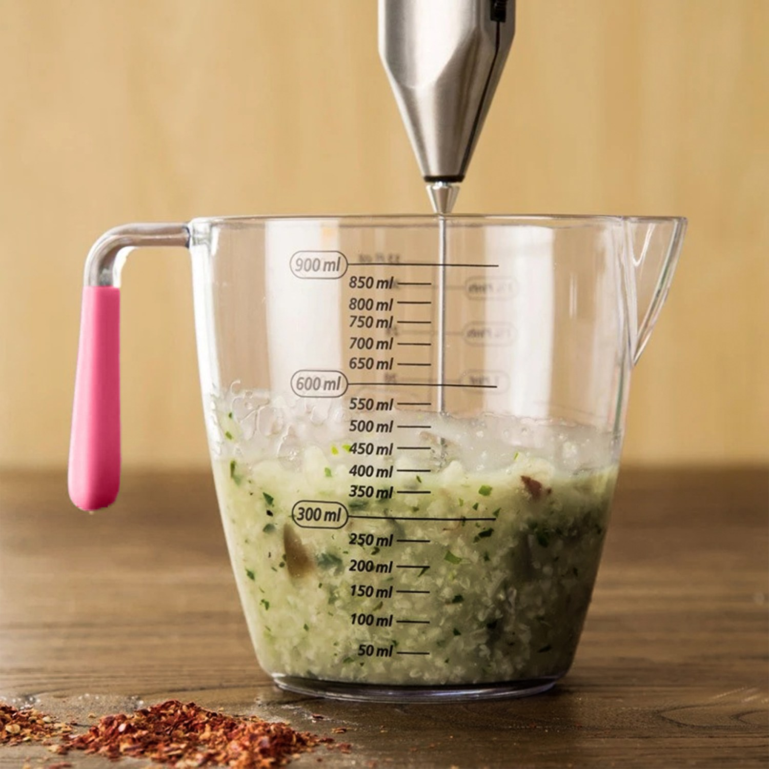 Ein Messbecher mit grüner Gemüsemischung, die mit einem Handmixer verrührt wird.