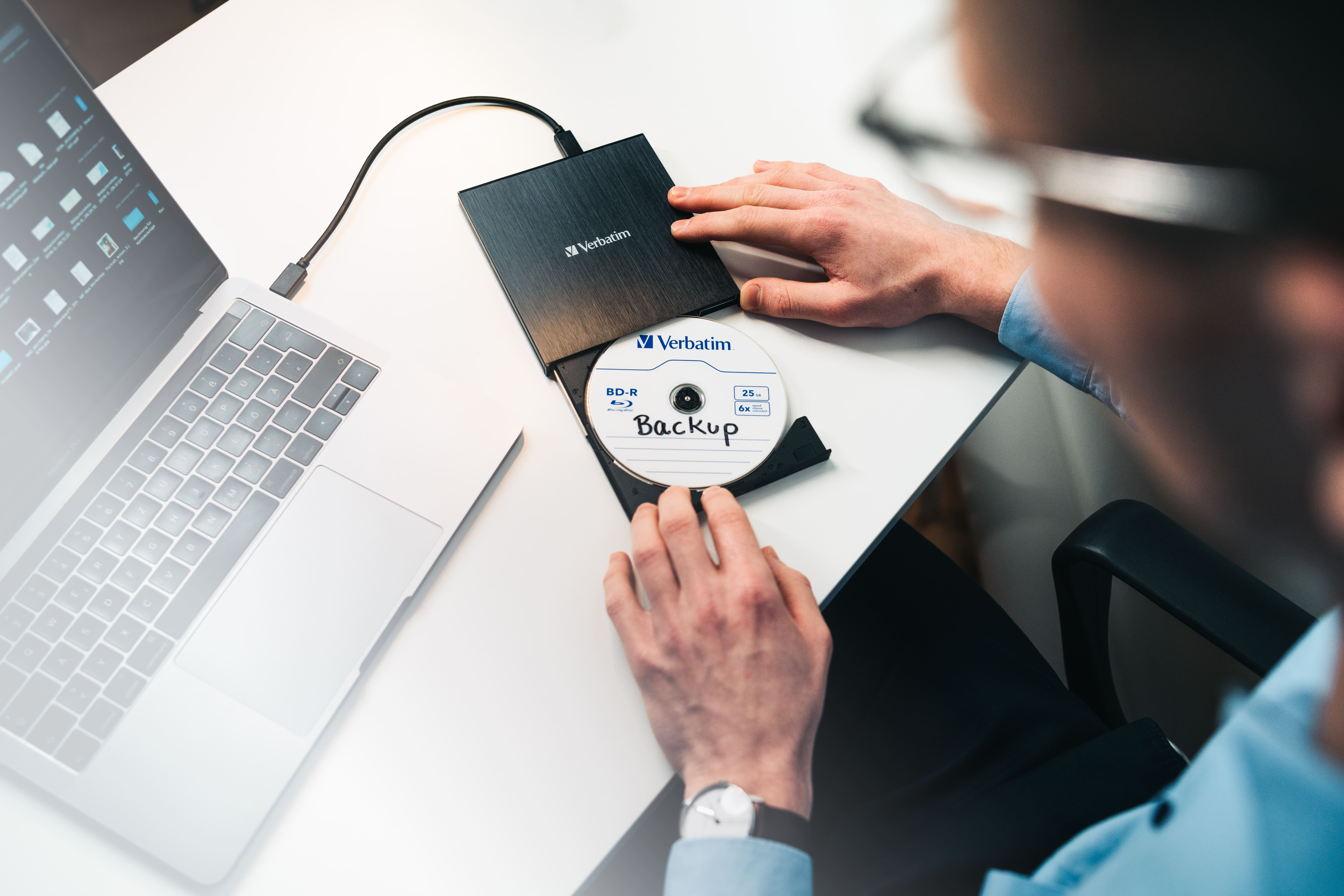 Osoba pracująca na laptopie, wkładająca płytę CD do zewnętrznego napędu Verbatim.