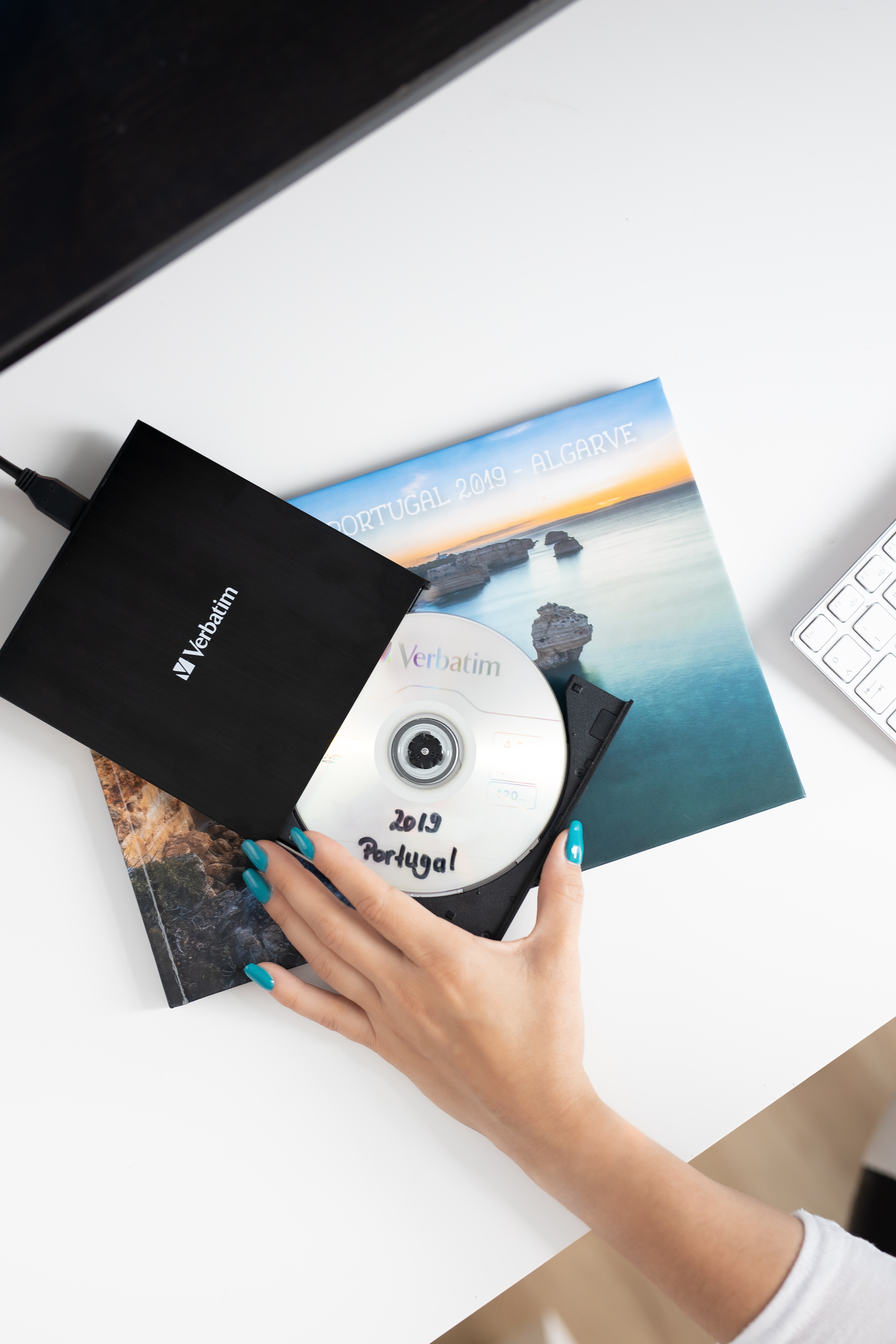 Kobieta używająca napędu CD na białym biurku z książką i klawiaturą.