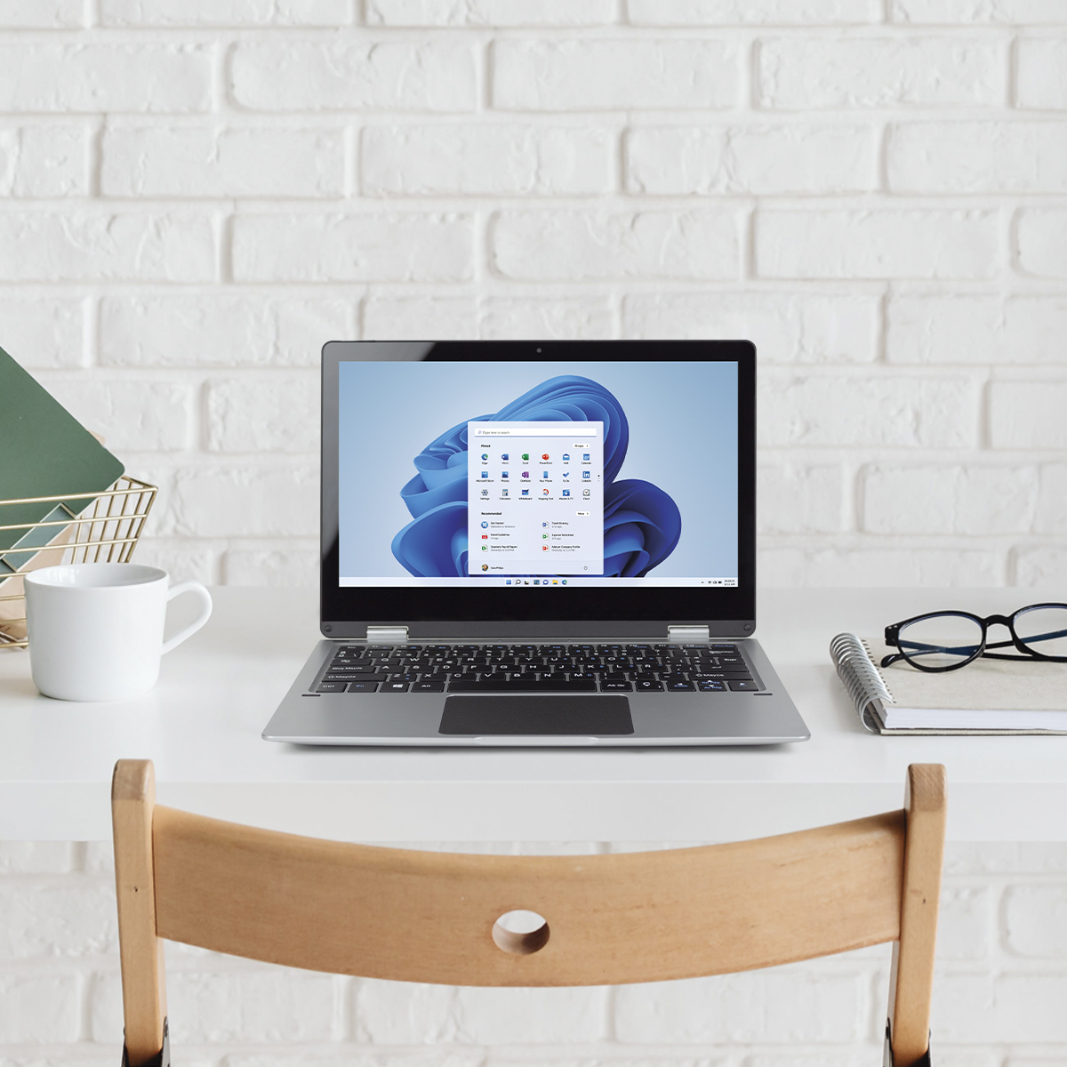 Laptop auf einem weißen Schreibtisch, geöffnet, zeigt eine Windows 11 Oberfläche, mit Tasse und Brille.