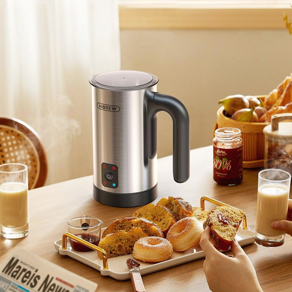 Srebrny spieniacz do mleka na stole z jedzeniem, w tym ciastkami, chlebem, dżemem i napojami.