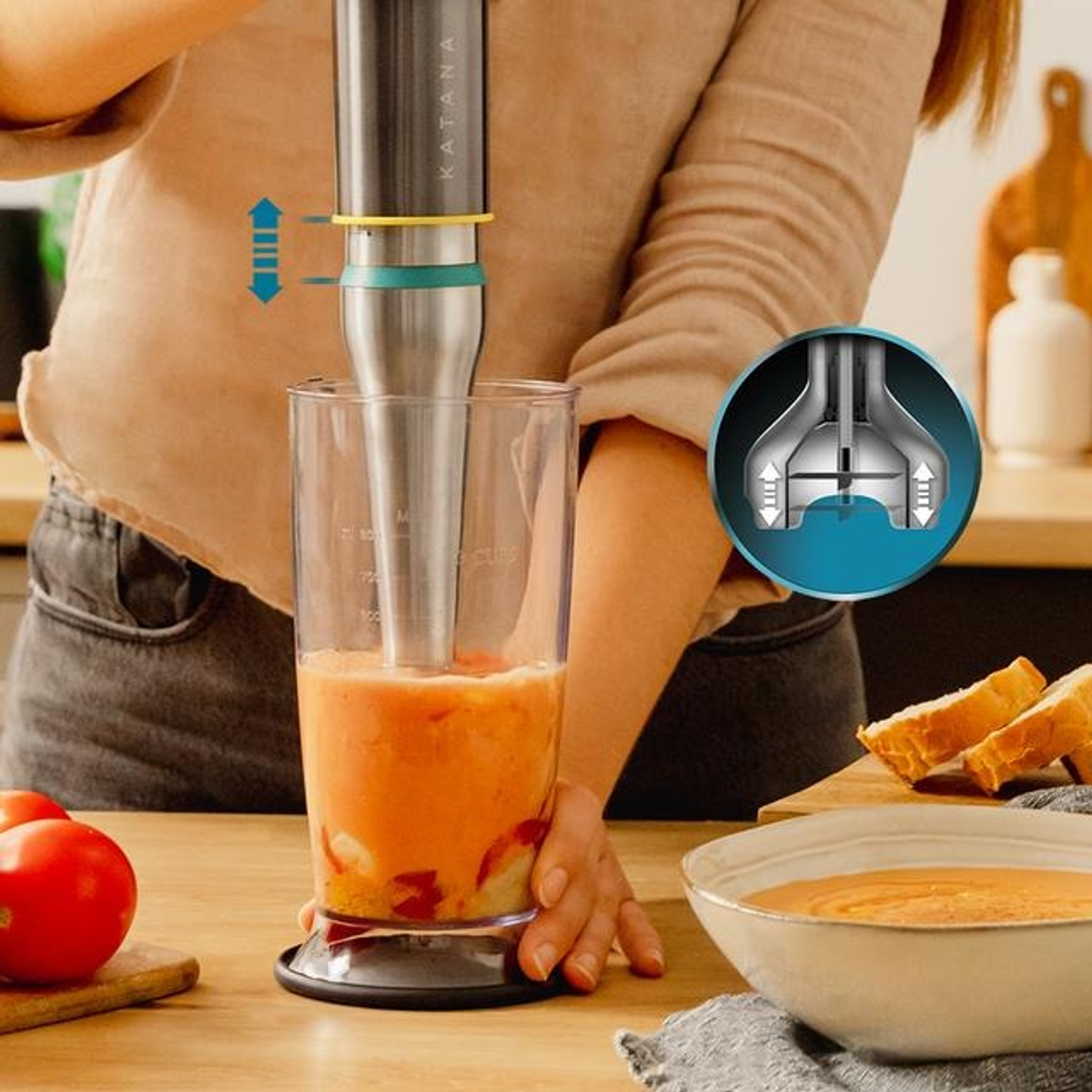 Osoba używająca blendera. Blender jest w szklance, a na stole z pomidorami stoi miska z zupą.