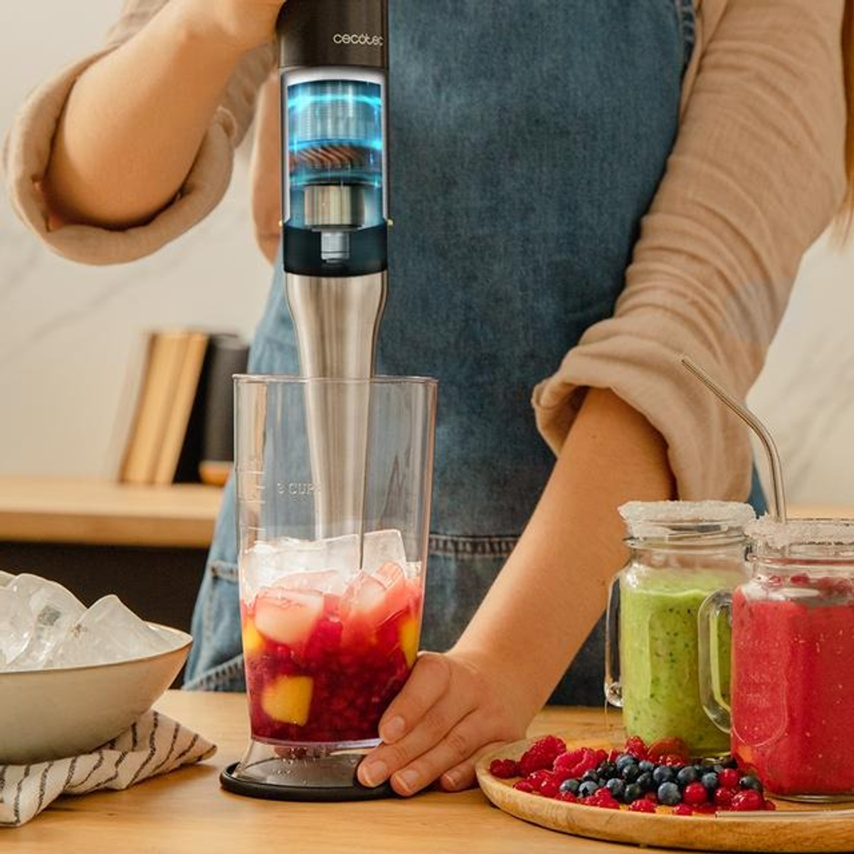 Osoba miksuje napój blenderem ręcznym. Składniki to lód i owoce.