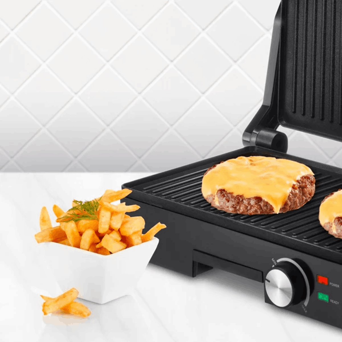 Grill mit Cheeseburgern und Pommes in einer Schüssel. Weißer Fliesen-Hintergrund sichtbar.