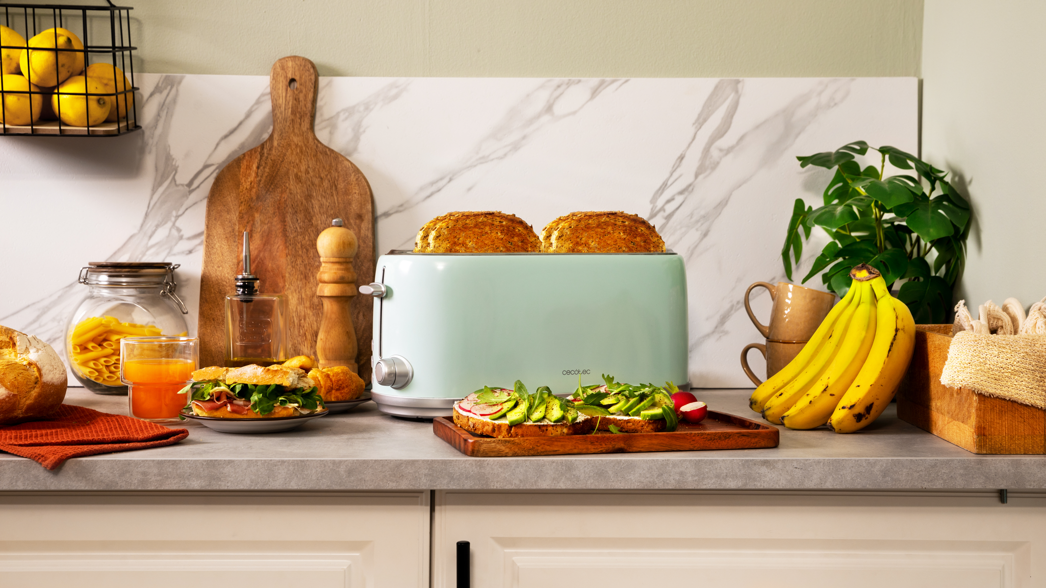Escena de cocina con tostadora, comida e ingredientes. Incluye pan, sándwiches, plátanos y una planta.