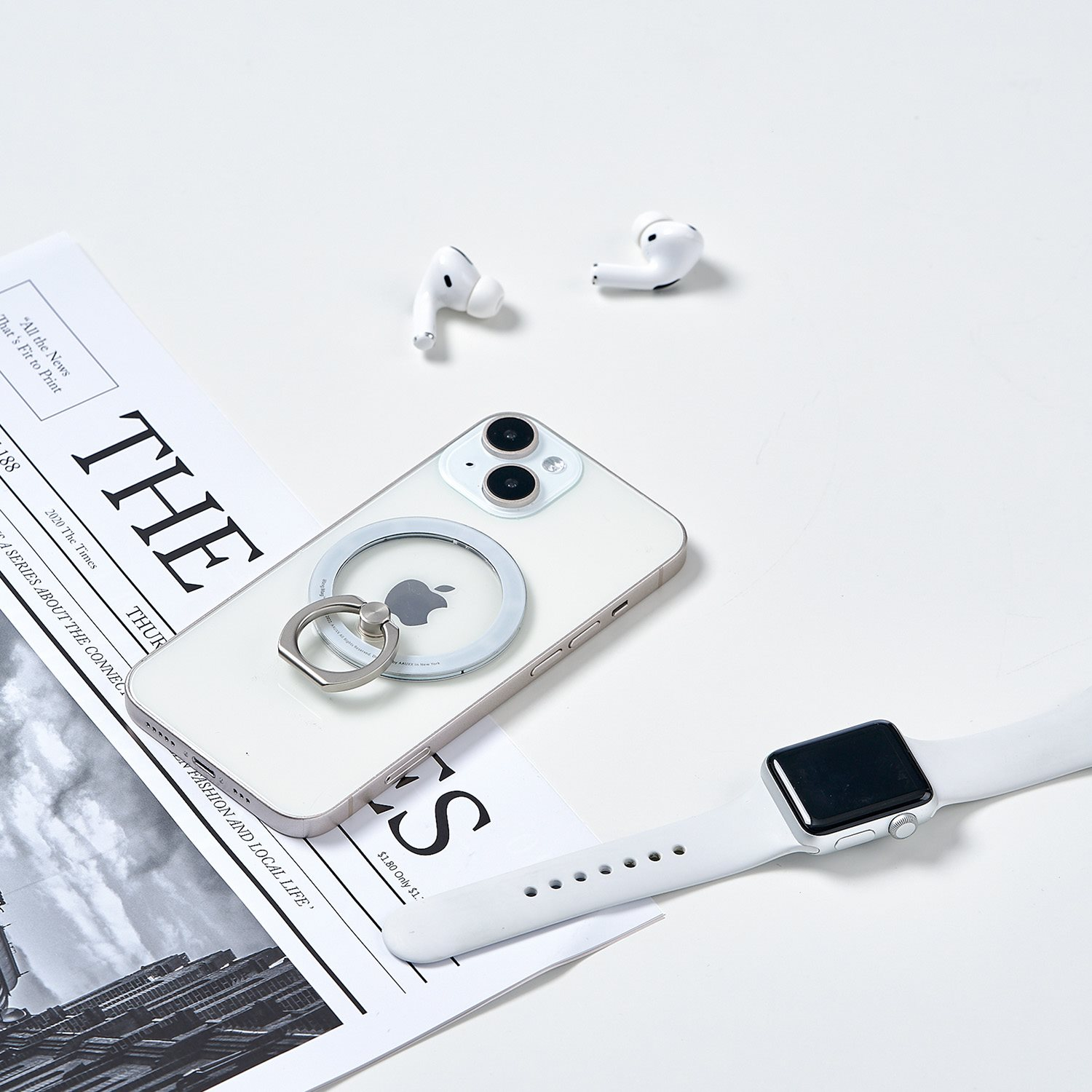 iPhone, AirPods und Apple Watch auf weißer Oberfläche neben einer Zeitung.
