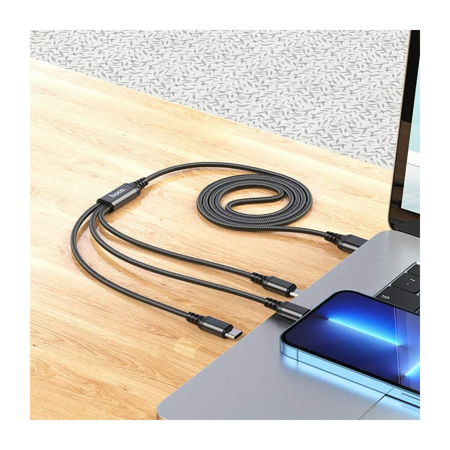Ein schwarzes USB-C-Kabel mit drei Anschlüssen, das an einen Laptop und ein Smartphone angeschlossen ist.