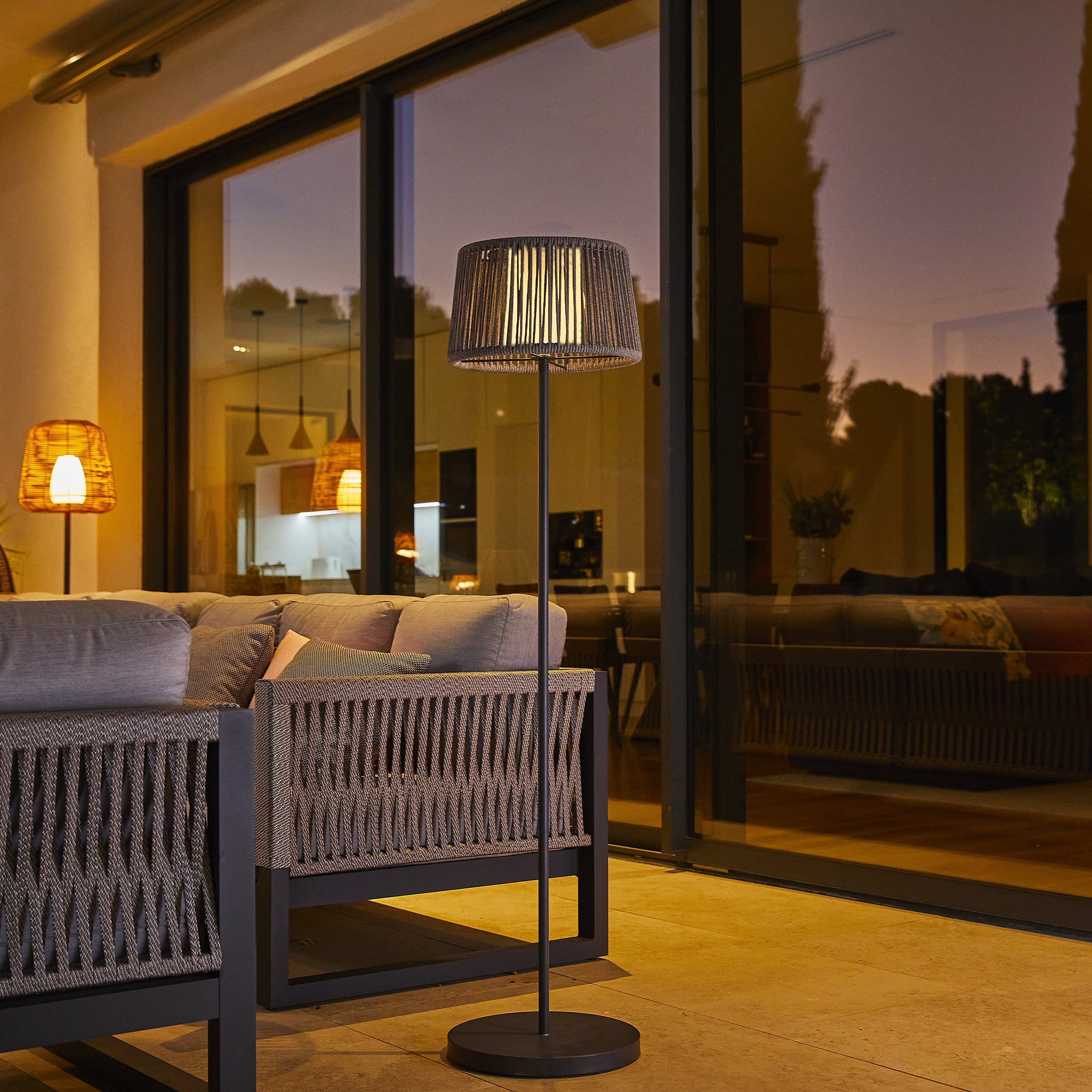 Eine Außenszene mit einer Stehlampe und einem Sofa. Die Lampe hat einen gewebten Schirm.