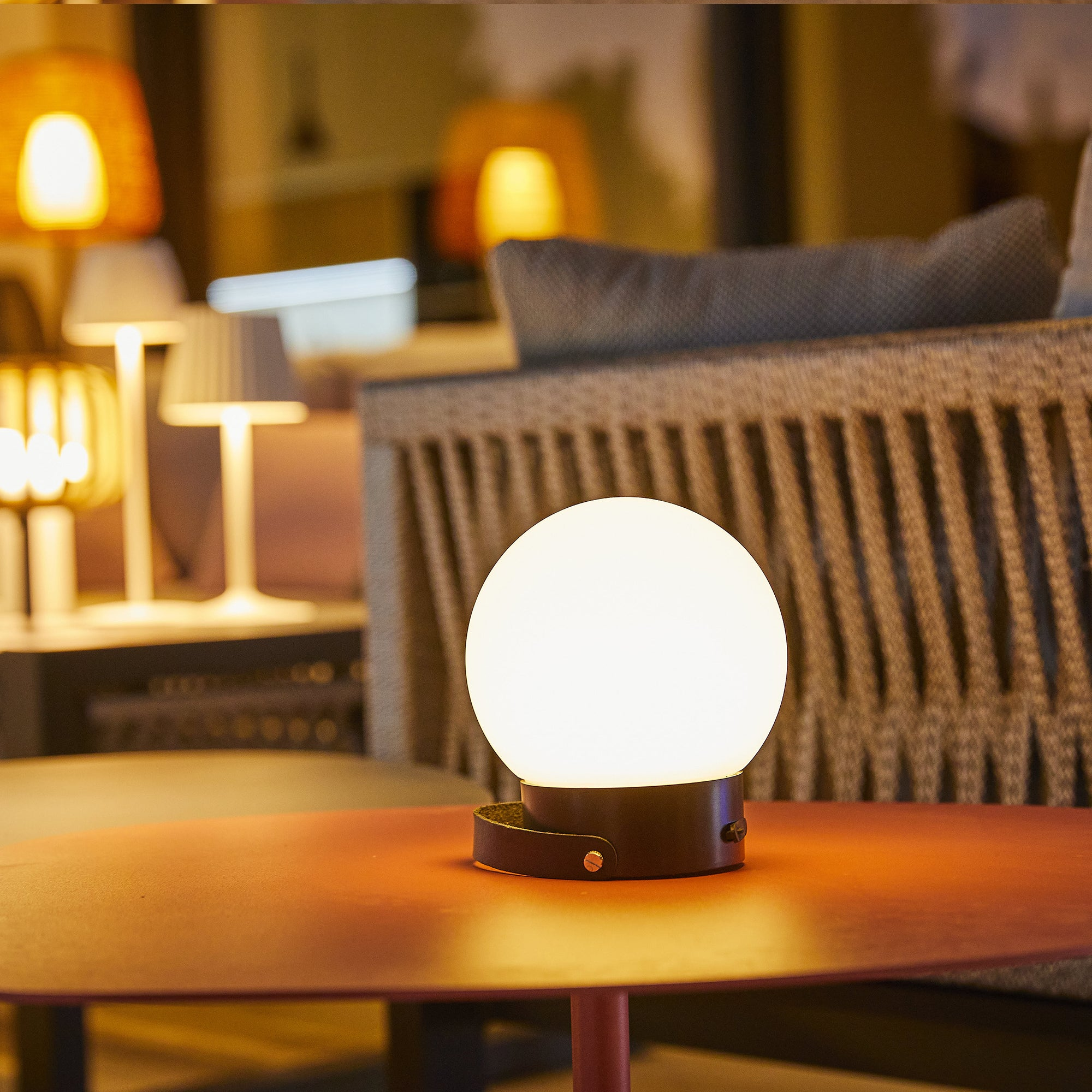 Eine beleuchtete Tischlampe mit weißem Globusschirm auf einem roten Tisch. Weitere Lampen im Hintergrund.
