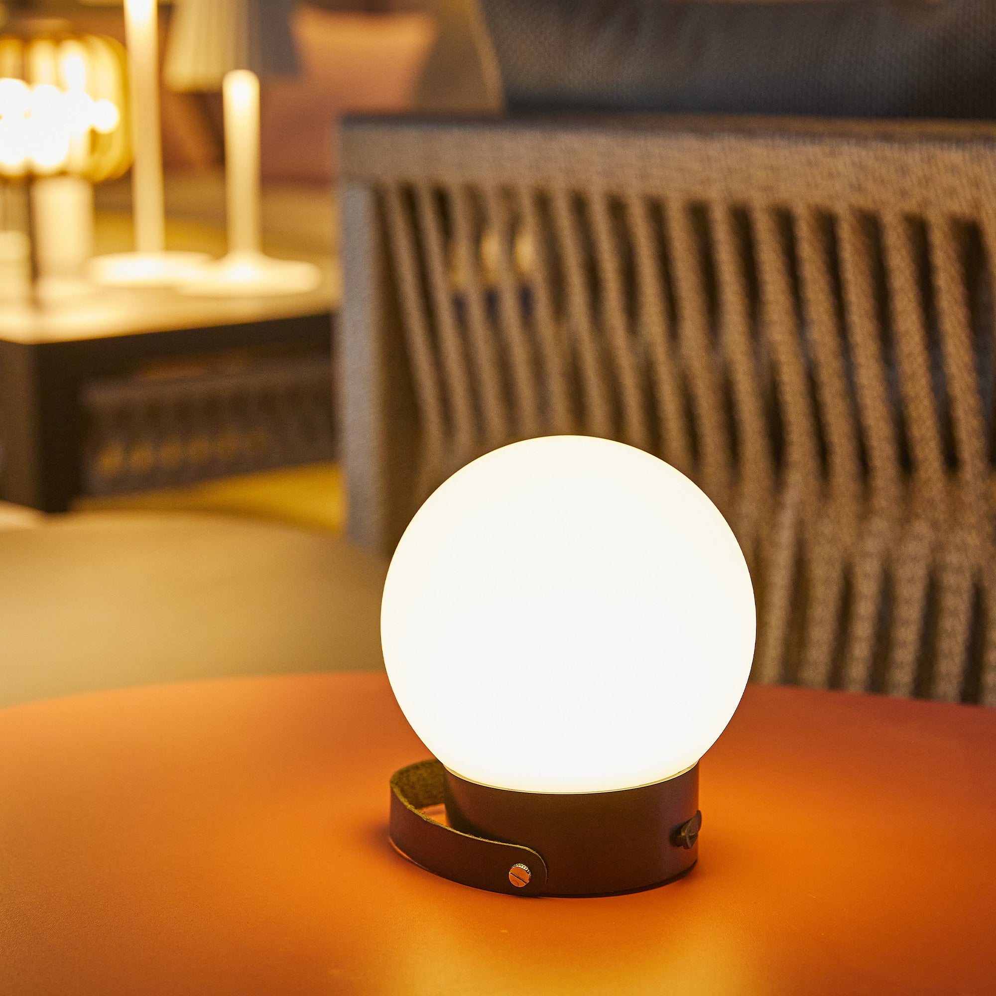 Runde weiße Lampe auf einem roten Tisch. Schwarzer Sockel mit Riemen. Der Hintergrund ist unscharf.