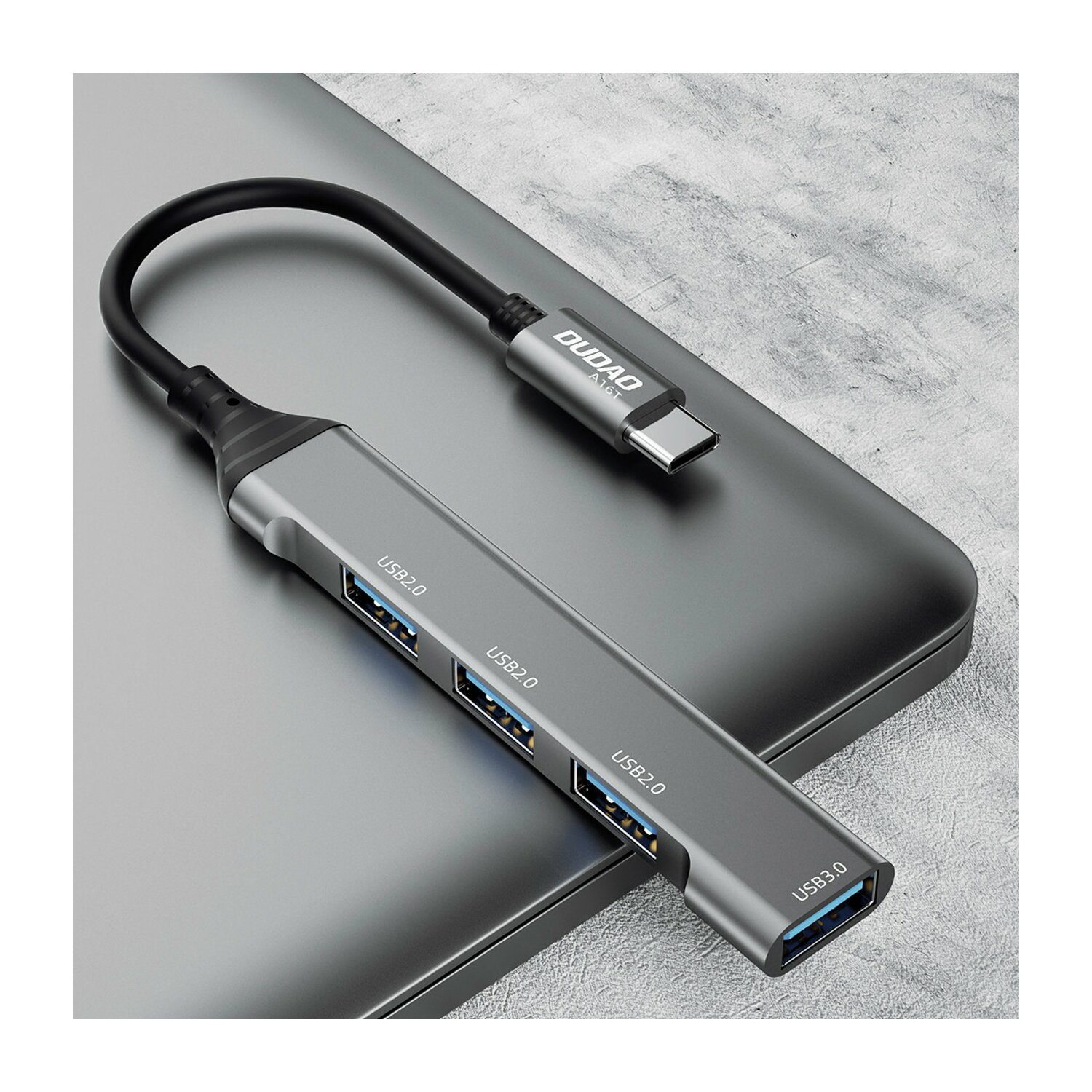 Un hub USB grigio con quattro porte USB e un connettore USB-C. È su una superficie grigia.