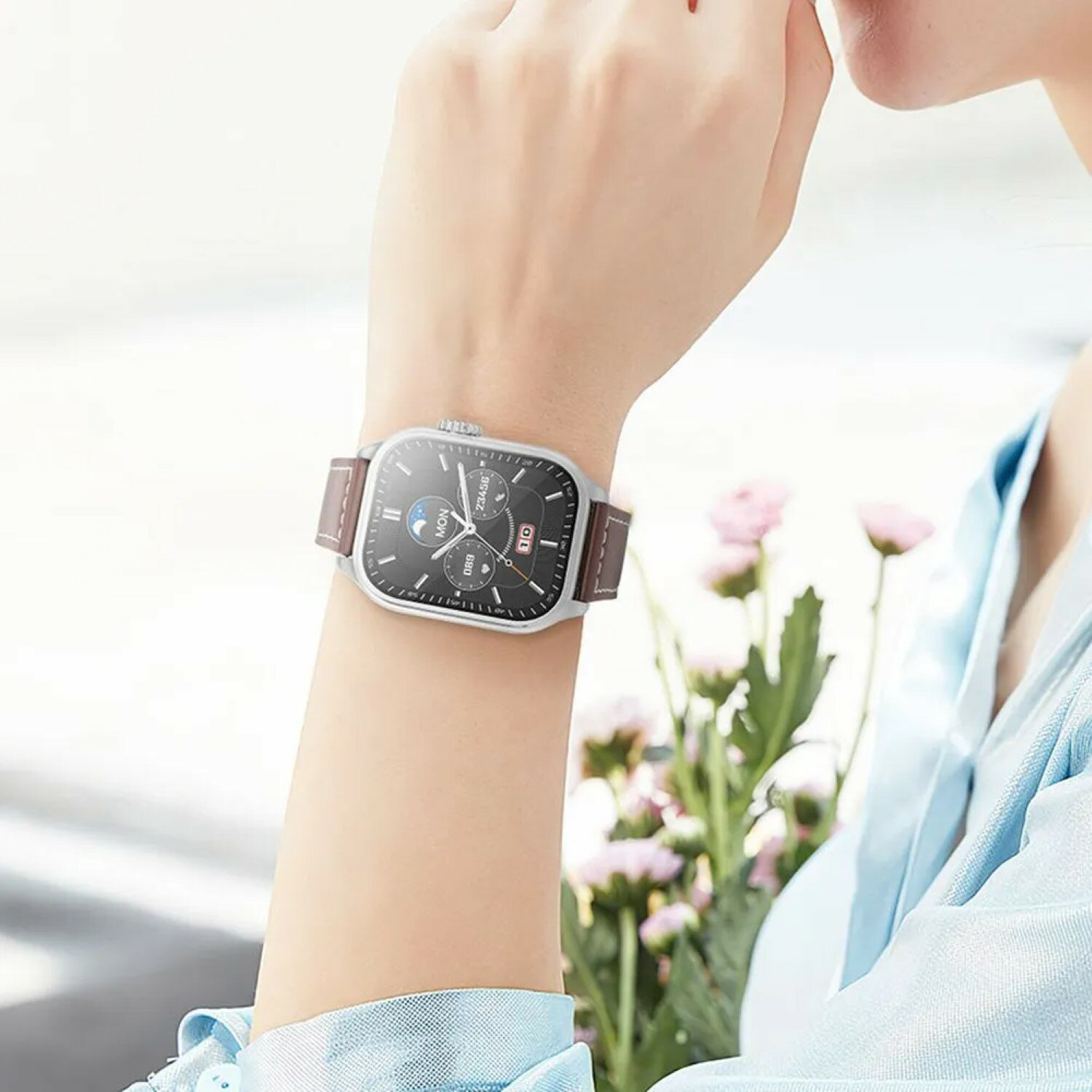 Handgelenk einer Frau mit silberner Uhr und braunem Lederarmband.