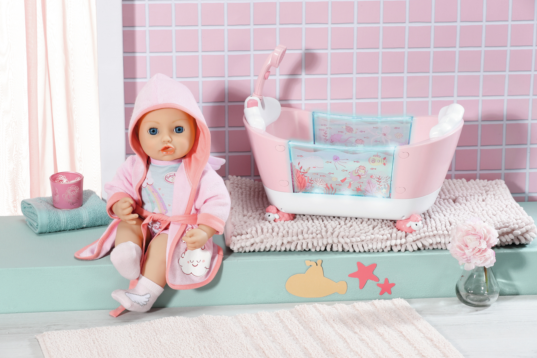 Babypuppe im rosa Bademantel sitzt neben einer rosa Wanne. Handtuch und Blumen in der Nähe.