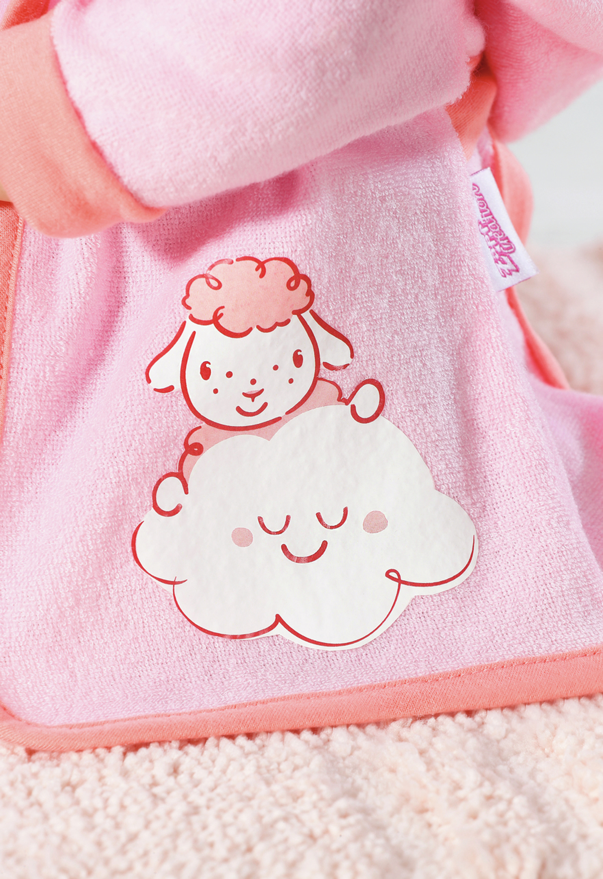 Eine rosa Puppe mit einem Lamm- und Wolkendesign auf ihrem Lätzchen wird gezeigt. Der Hintergrund ist rosa.