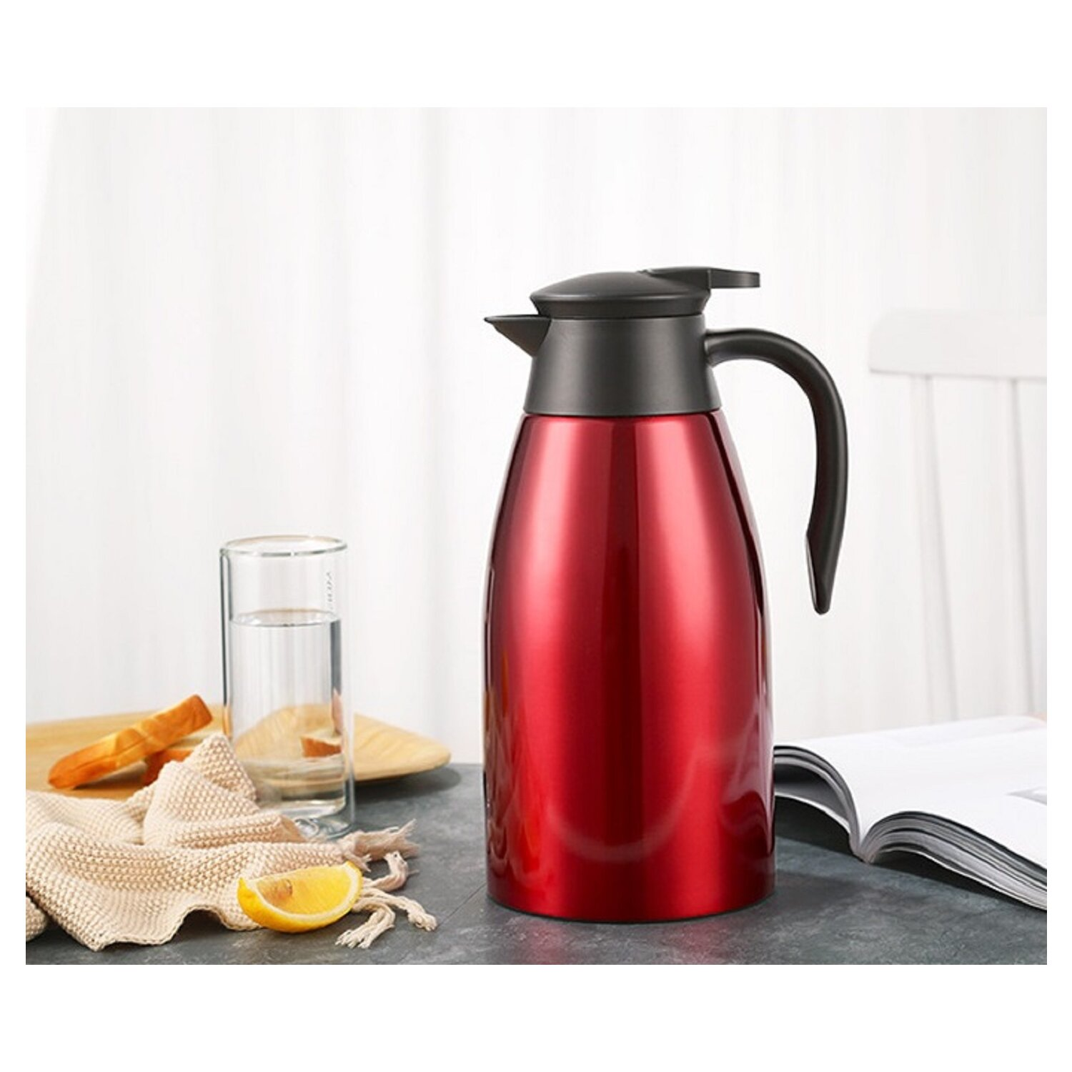 Roter Isolier-Thermos. Ein schwarzer Deckel und Griff. Ein Glas und eine Zitronenscheibe liegen auf dem Tisch.