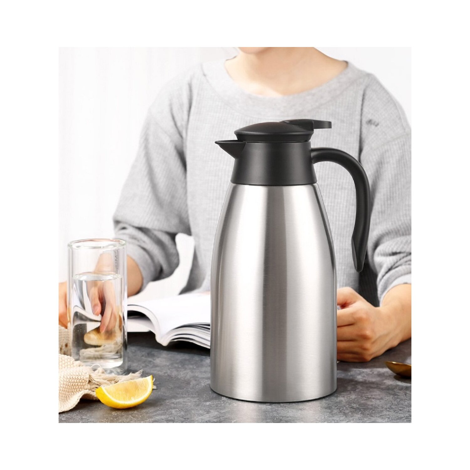 Thermoskanne aus Edelstahl. Eine Person hält sie neben einem Glas Wasser.