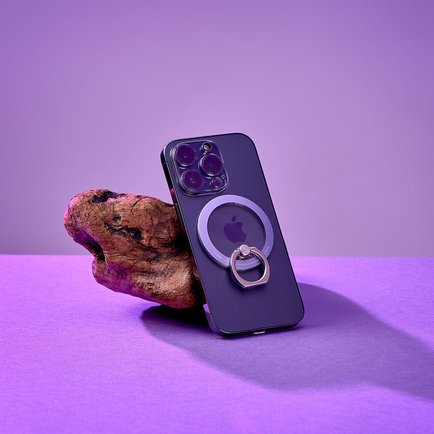 Schwarzes Telefon mit Ringhalterung auf Holzblock, violetter Hintergrund.