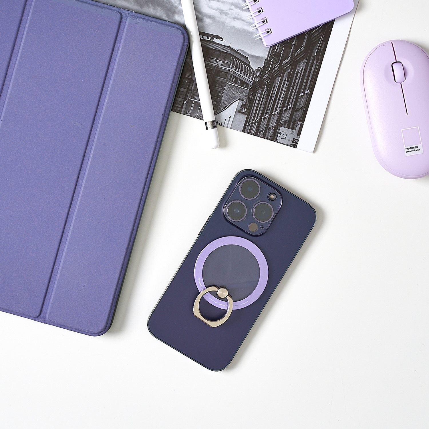 Lila Telefon mit Ringständer, Tablet, Maus und Notizblock auf weißem Schreibtisch.
