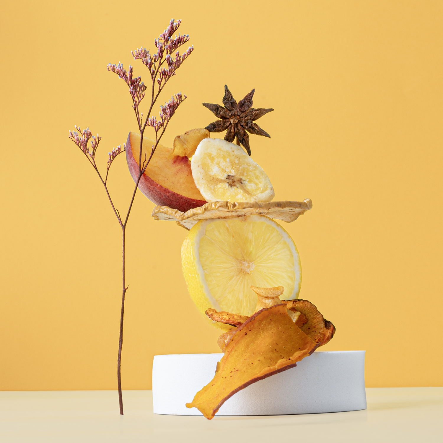 Frutta e spezie disposte su un blocco bianco su sfondo giallo, impilate verticalmente.