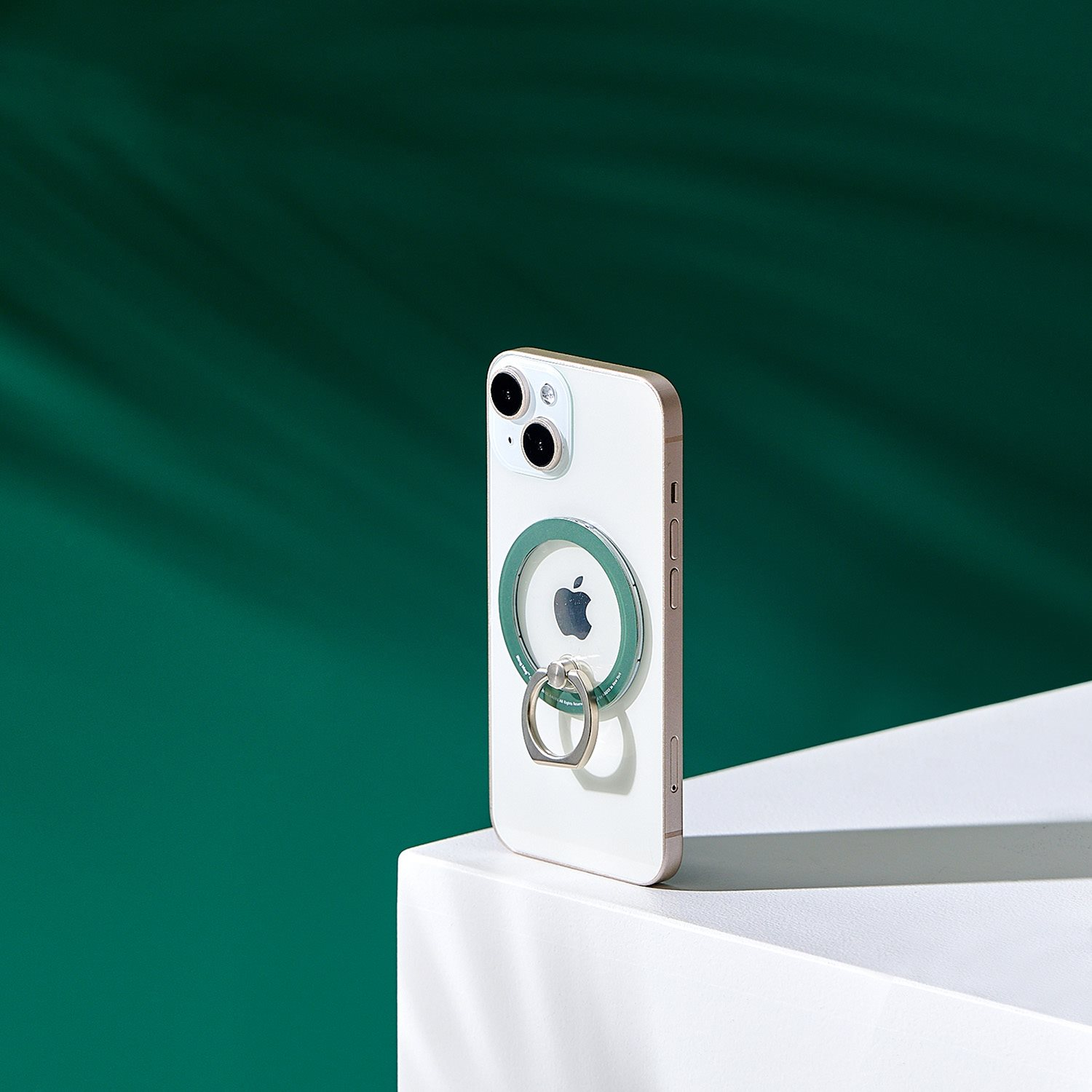Ein weißes iPhone mit grünem Ringhalter auf der Rückseite und grünem Hintergrund, auf weißer Oberfläche.