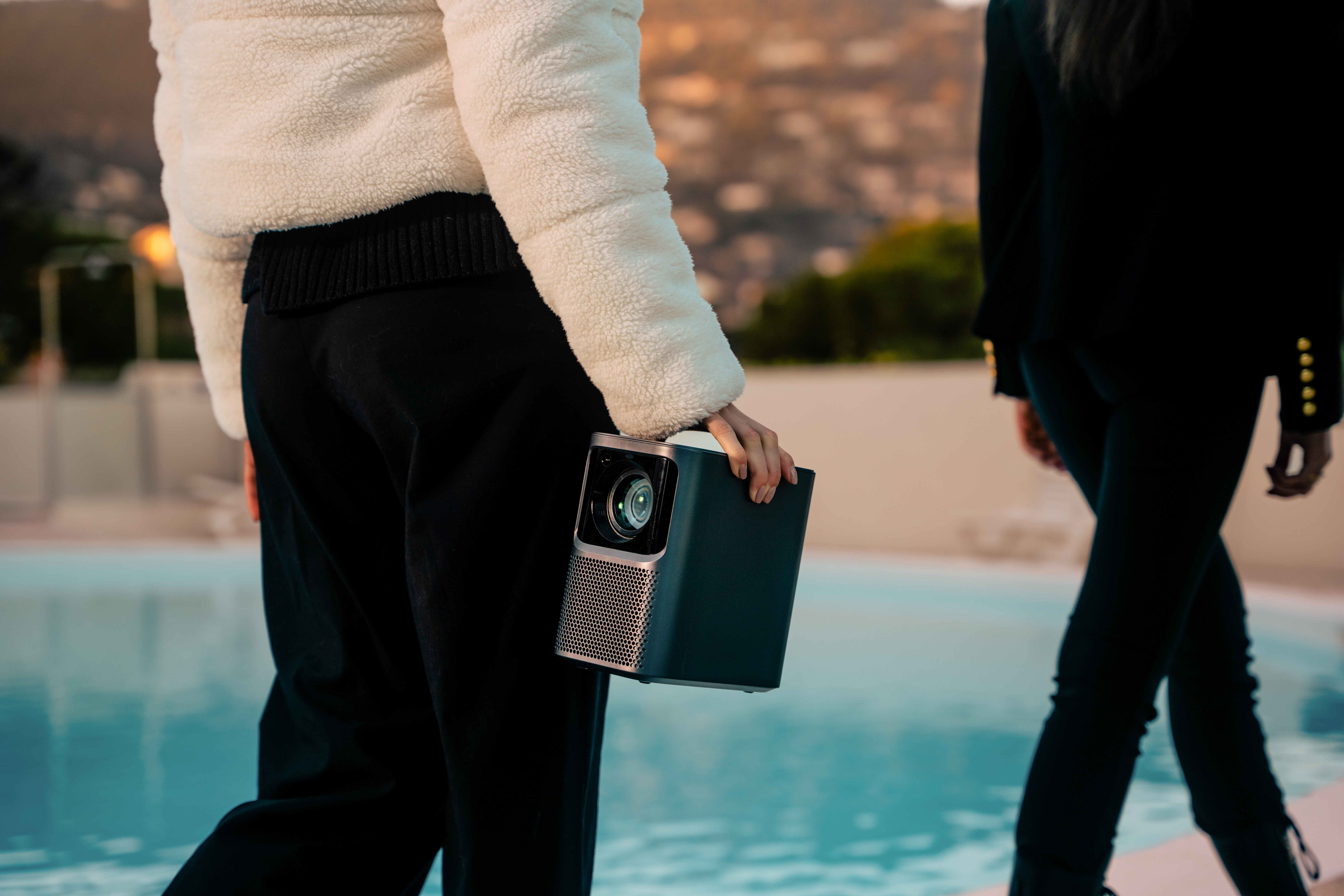 Osoba trzyma przenośny projektor, druga idzie w pobliżu basenu.