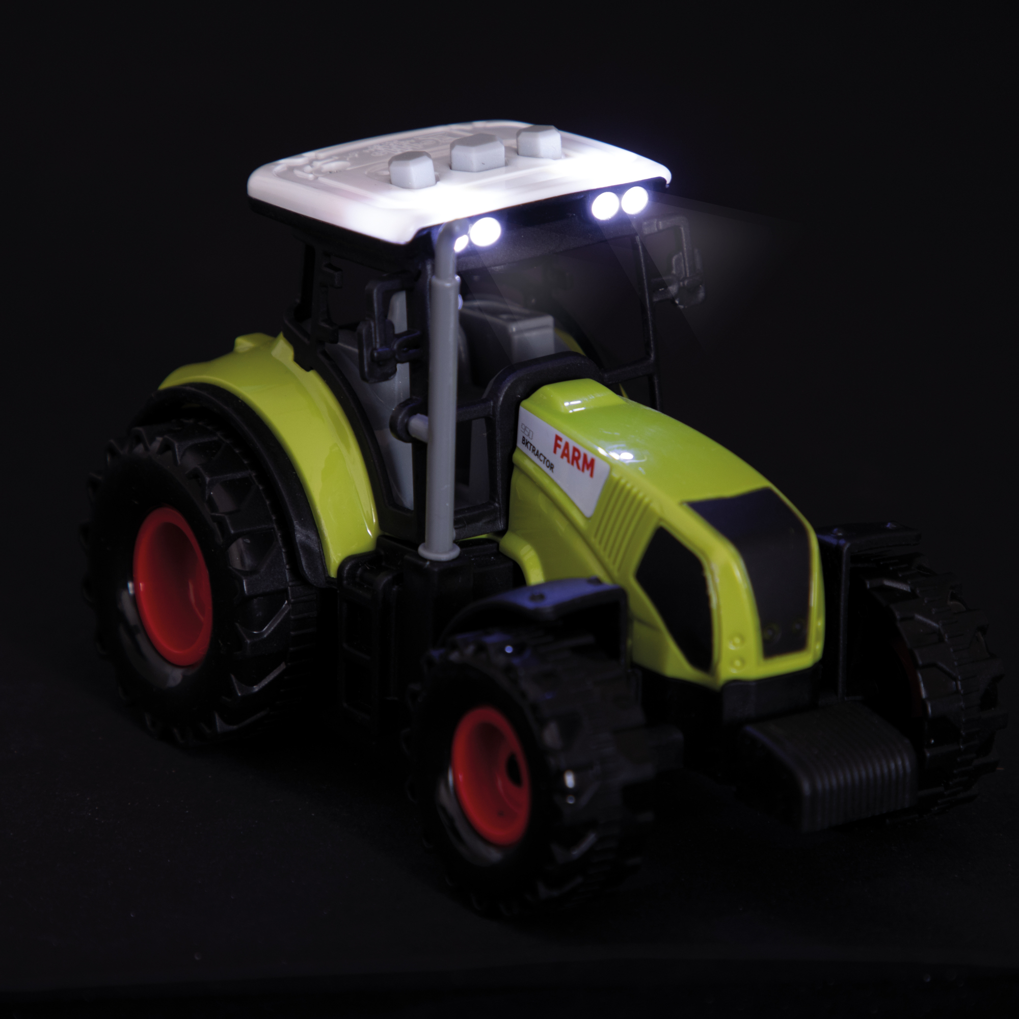 Ein Spielzeugtraktor mit grünem Gehäuse, weißem Dach und roten Rädern. Er hat Lichter an. Dunkler Hintergrund.