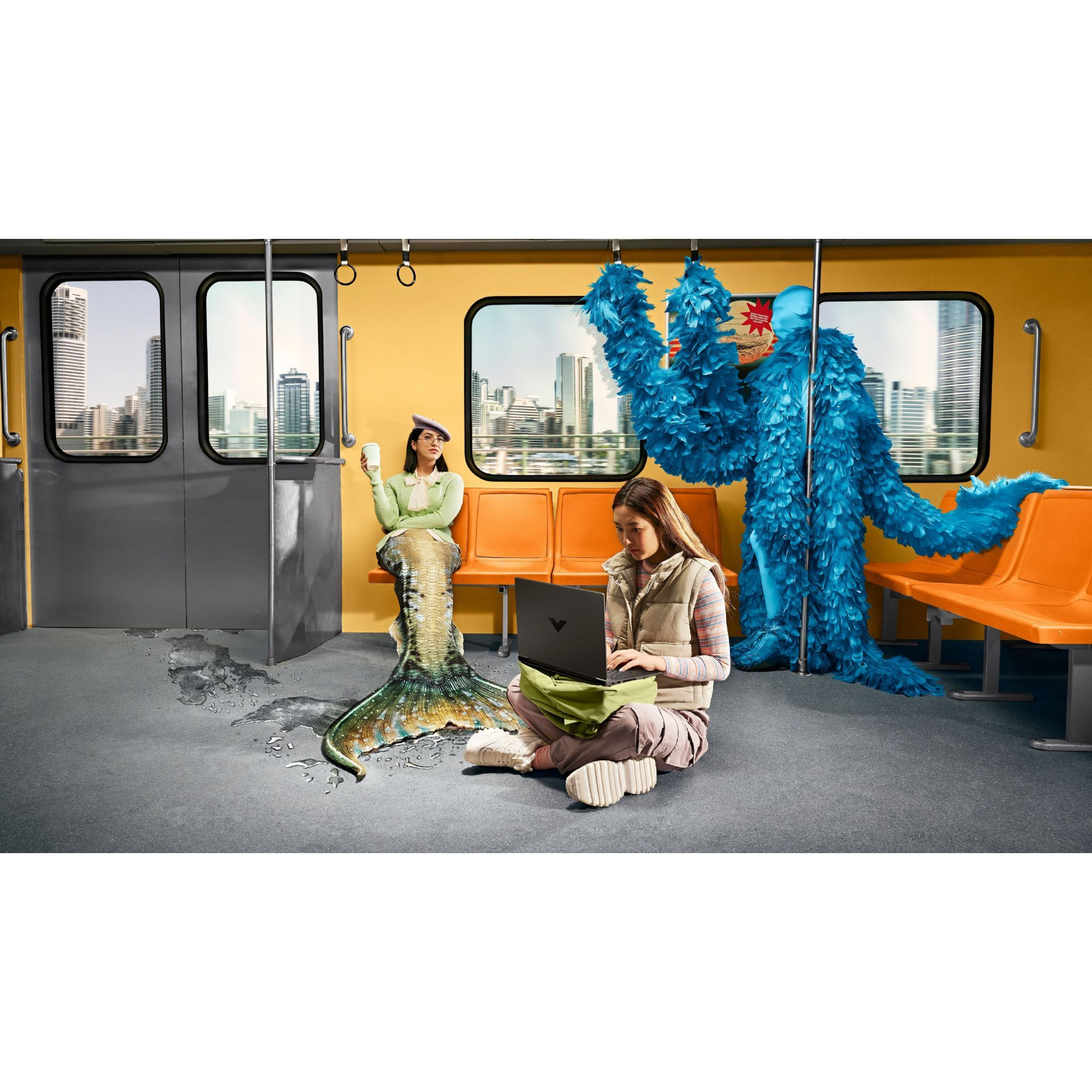 Una sirena y un monstruo azul peludo en un tren. Una persona usa una laptop, otra bebe té.