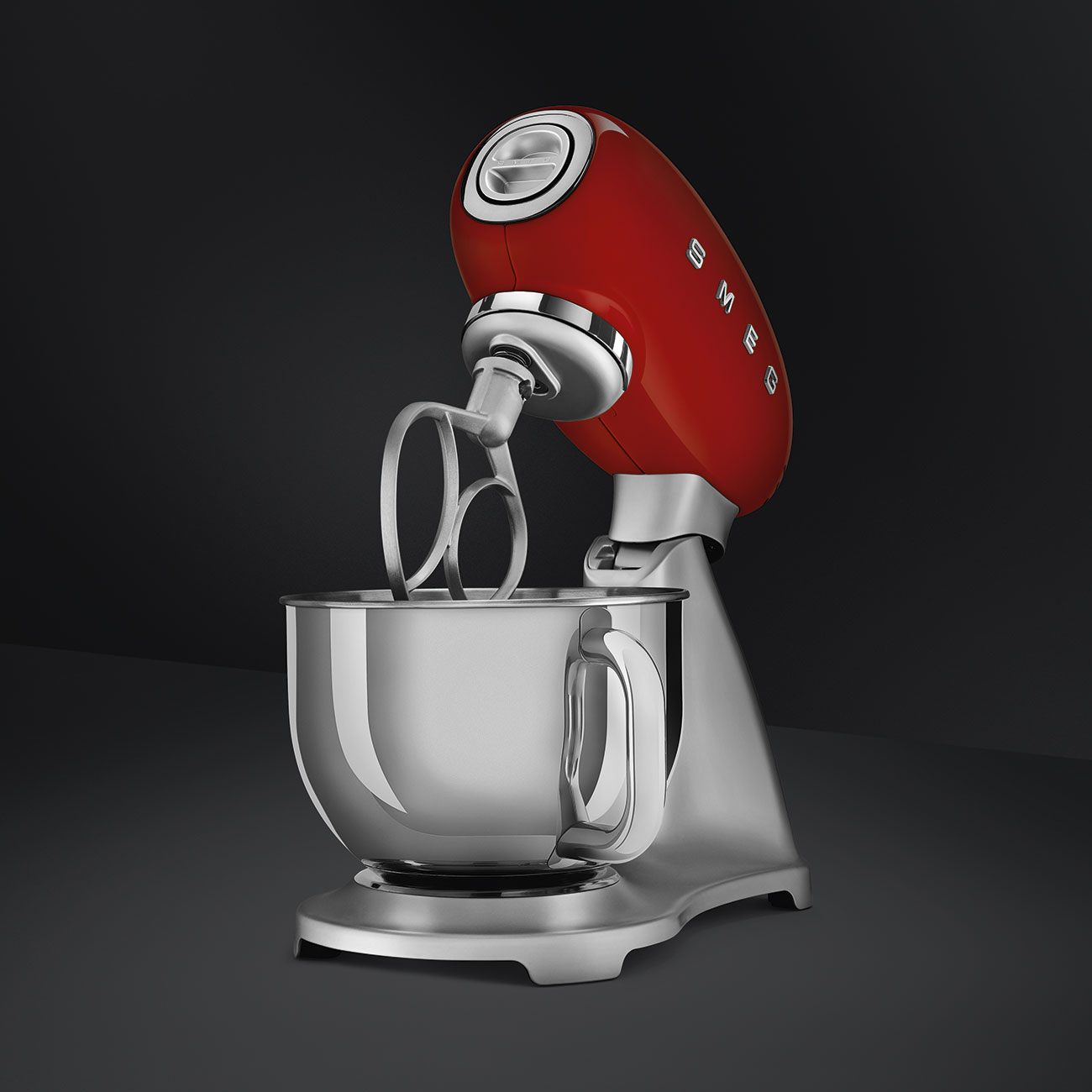 Roter Smeg-Küchenmixer mit Aufsätzen auf grauer Oberfläche mit dunklem Hintergrund.
