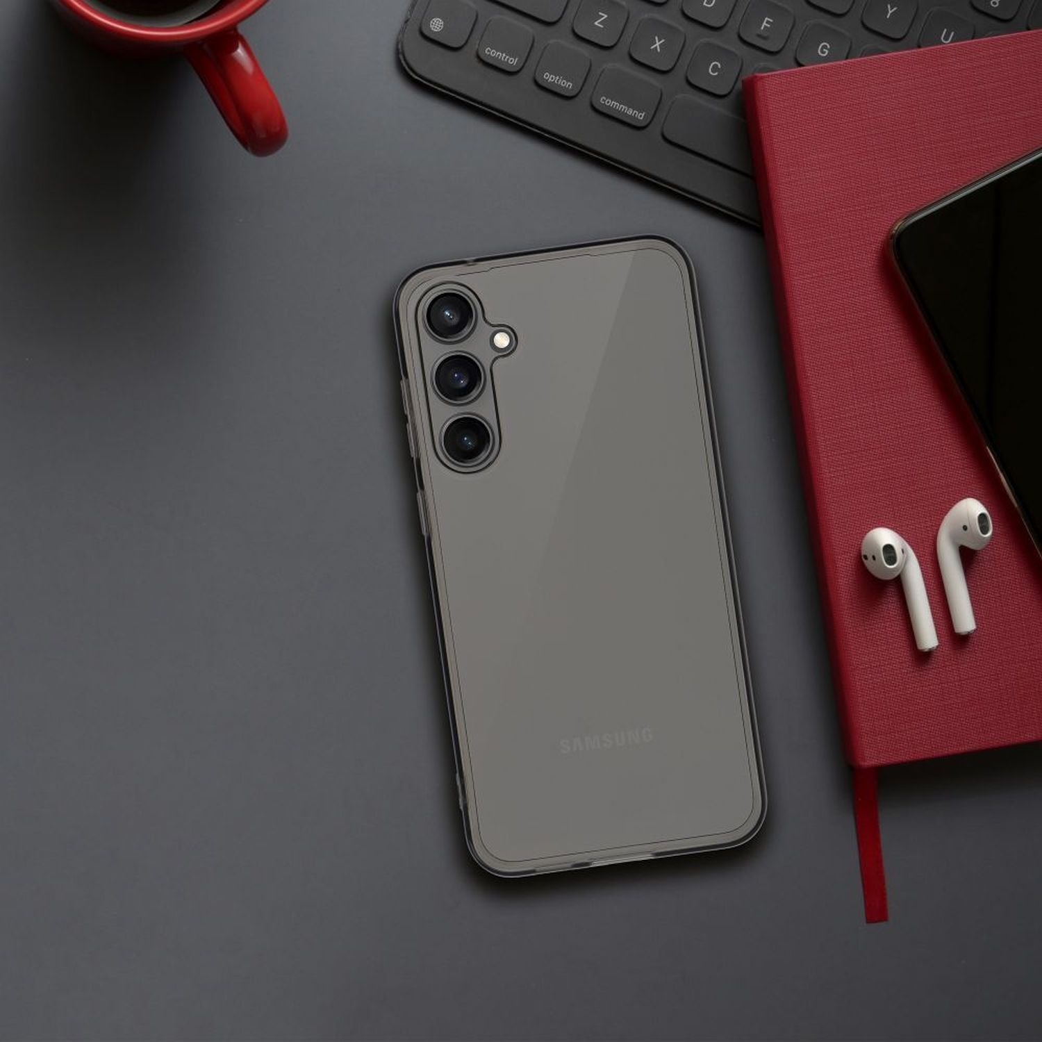 Telefono sulla scrivania, custodia trasparente, tastiera nera, quaderno rosso, cuffie e caffè.