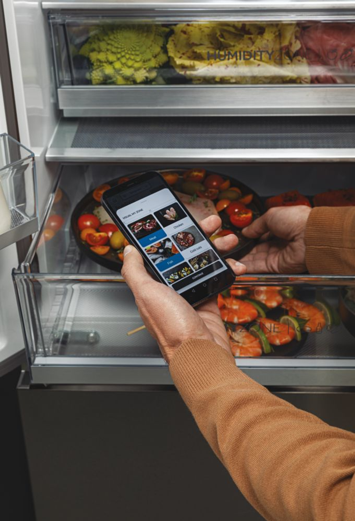 Mano sosteniendo un teléfono mostrando opciones de comida dentro de un refrigerador. El refrigerador contiene verduras y carne.