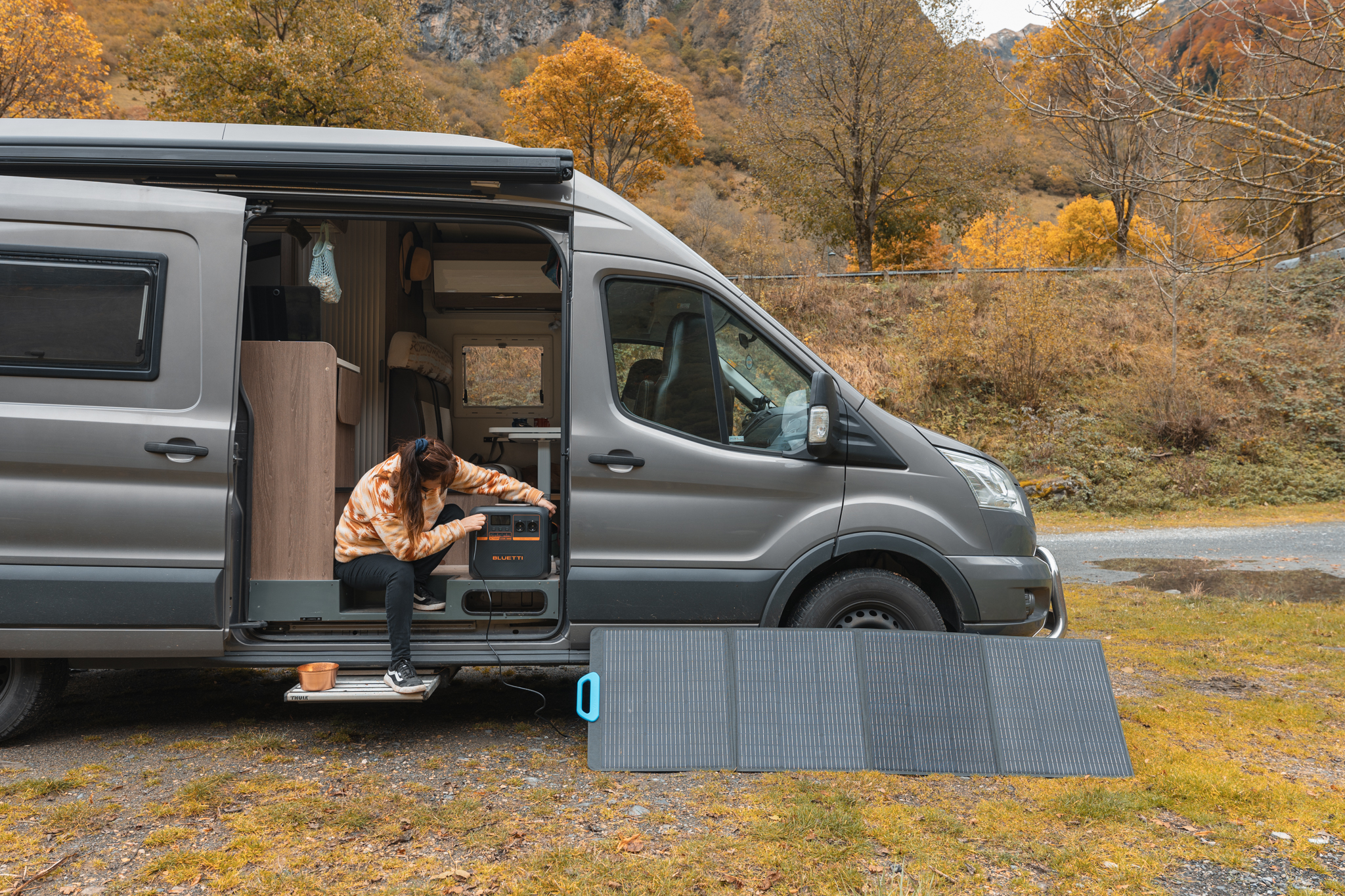 Kobieta obok szarego vana, ustawiająca czarny panel słoneczny i elektrownię.