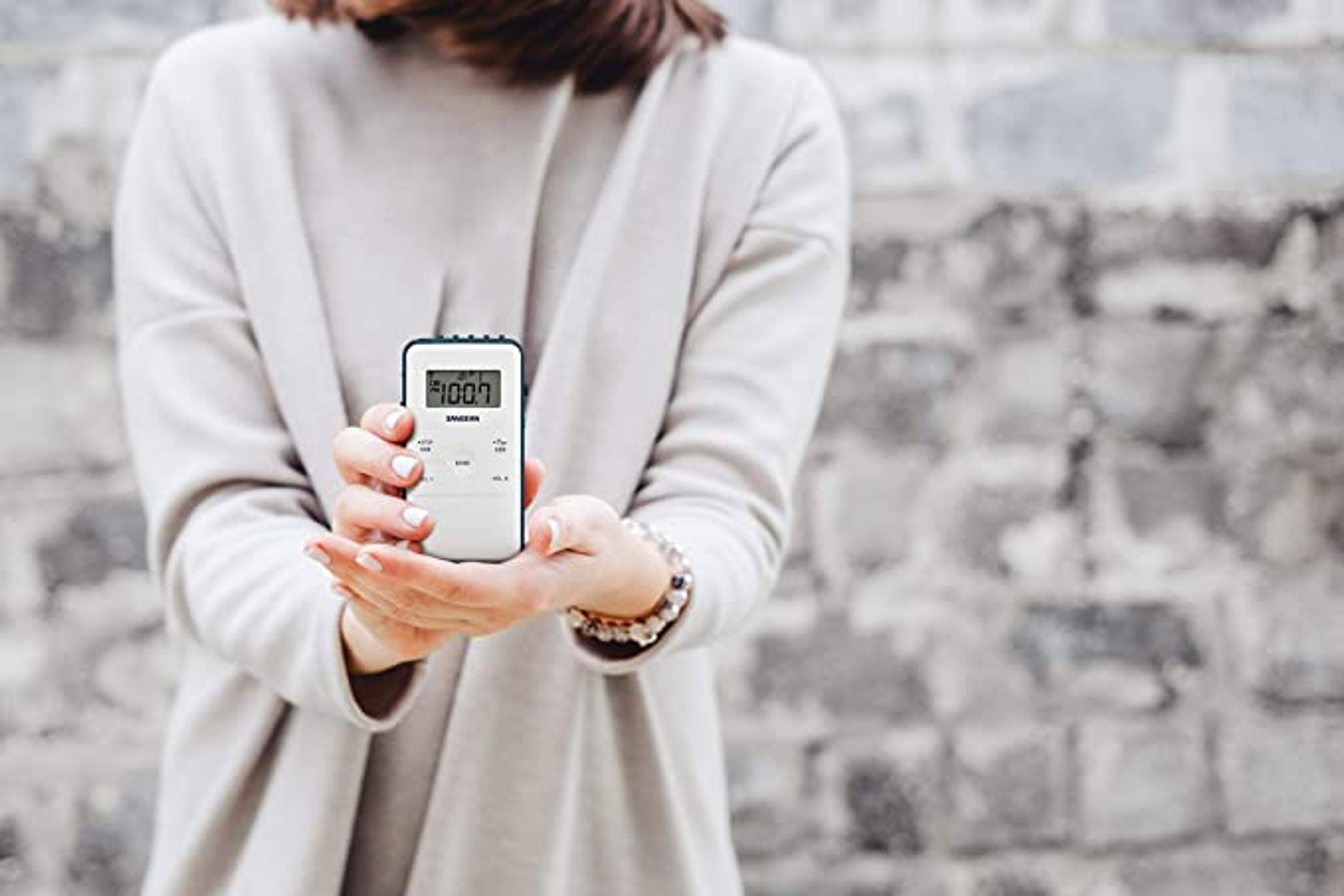 Osoba trzymająca białe radio cyfrowe z wyświetlaczem 100.7 FM.