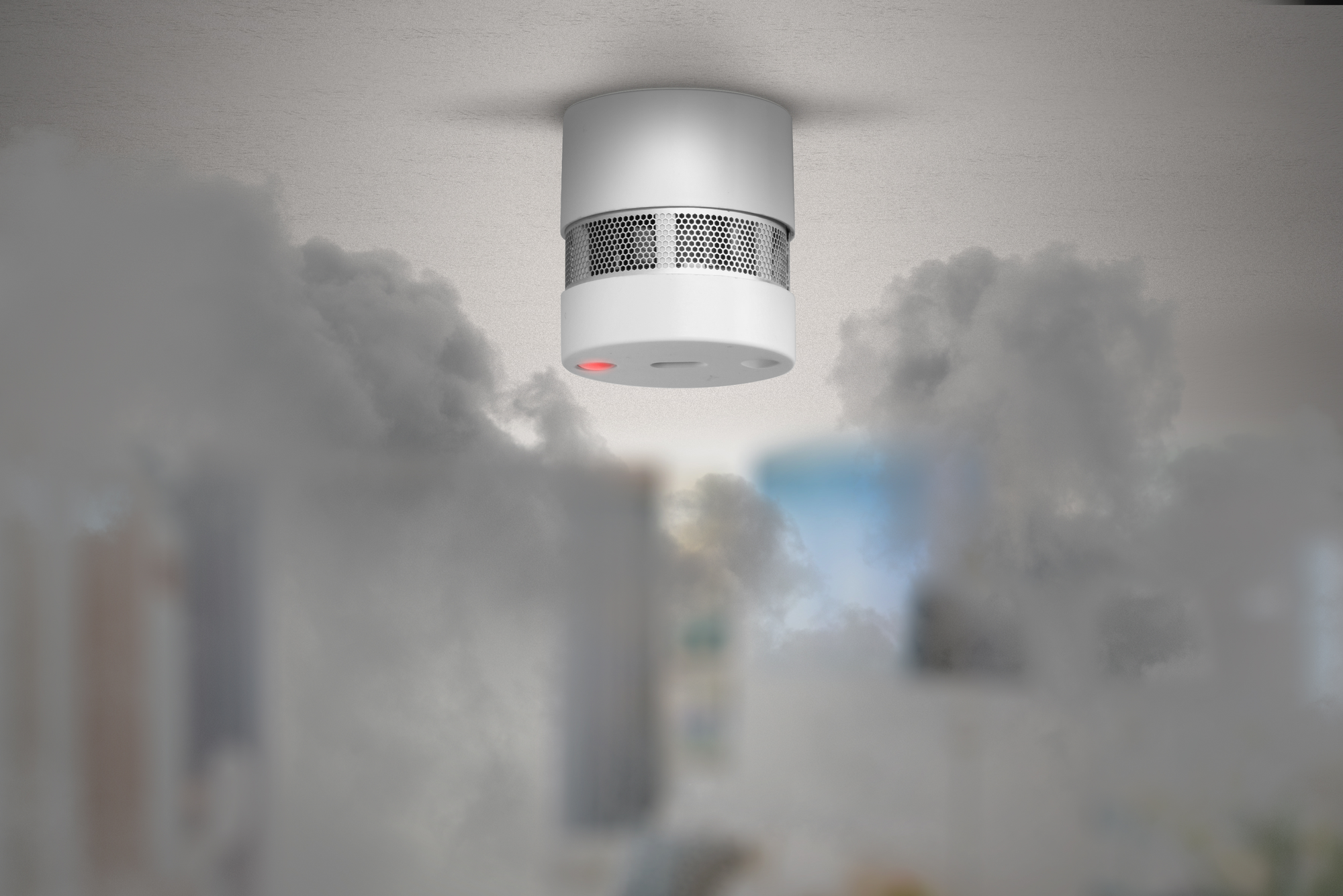Biały czujnik dymu na białym suficie, z dymem wypełniającym pomieszczenie i zasłaniającym tło.