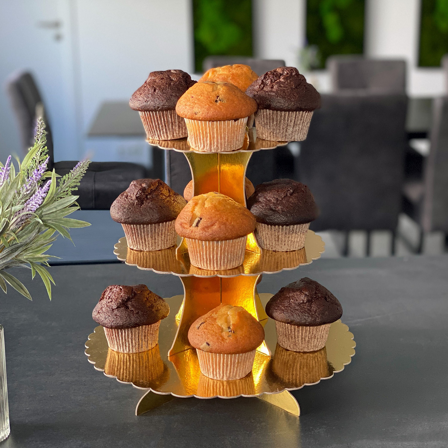 Neun Cupcakes auf einem dreistöckigen Goldständer, verschiedene Geschmacksrichtungen.